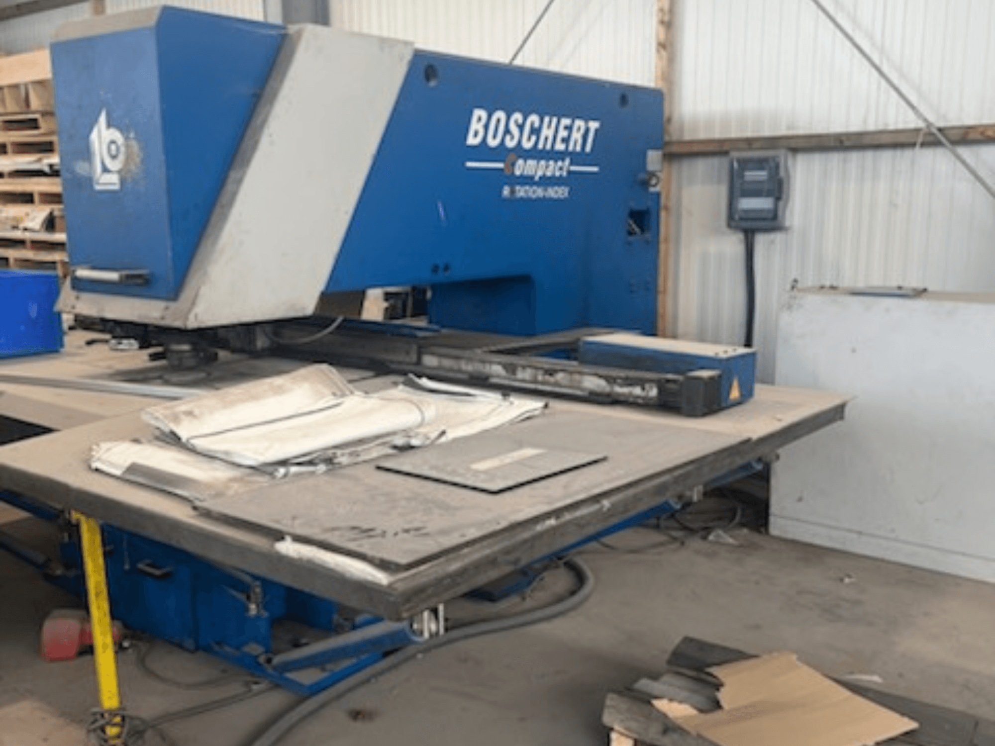 Punzonatrice CNC BOSCHERT COMPACT 1000 in un'officina, con vista frontale e lamiere sul tavolo di lavoro.