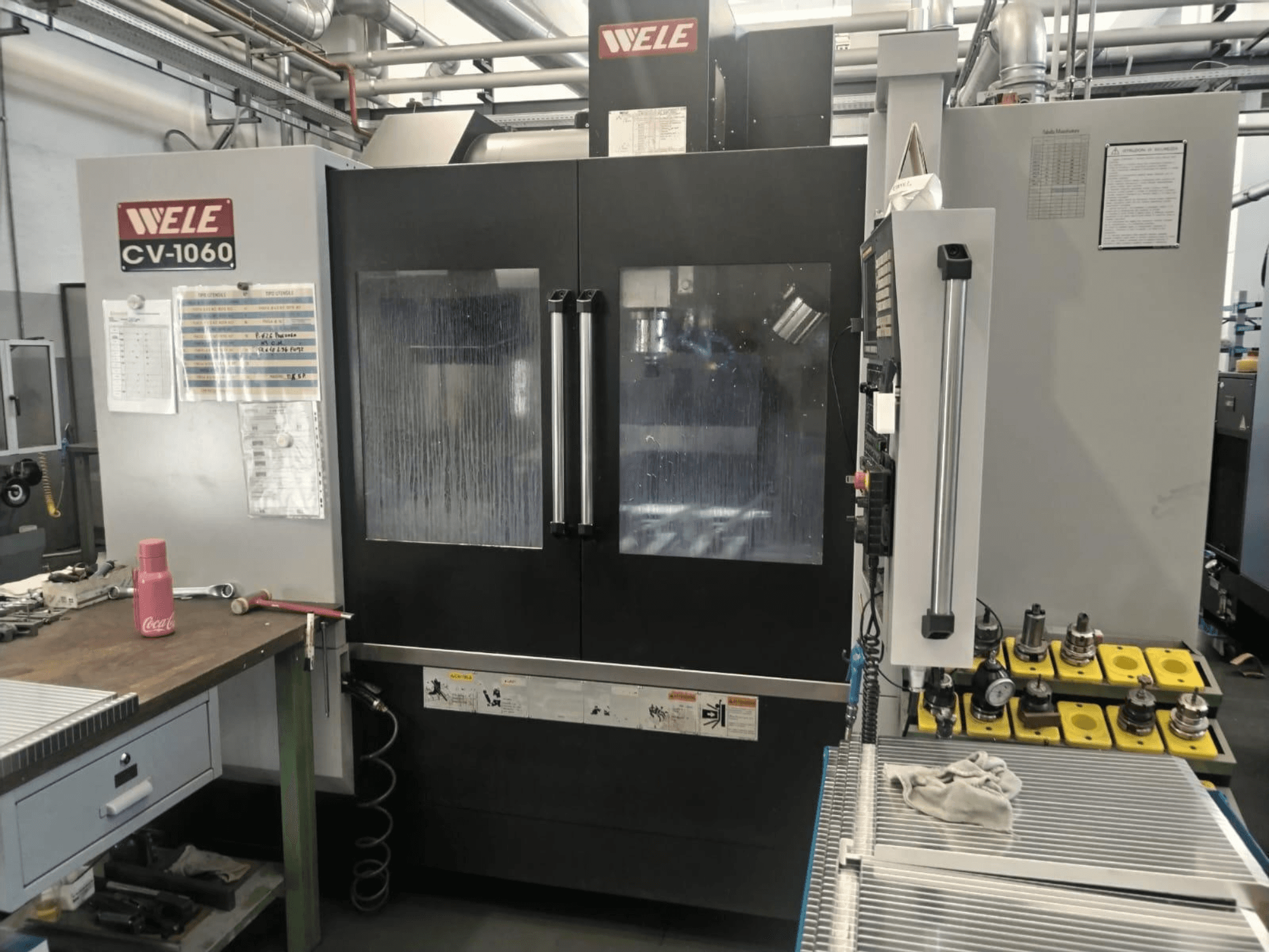 Centro di lavorazione verticale Wele CV-1060, vista frontale, con pannello di controllo e area di lavoro visibile; include utensili accessori ed etichette di sicurezza.