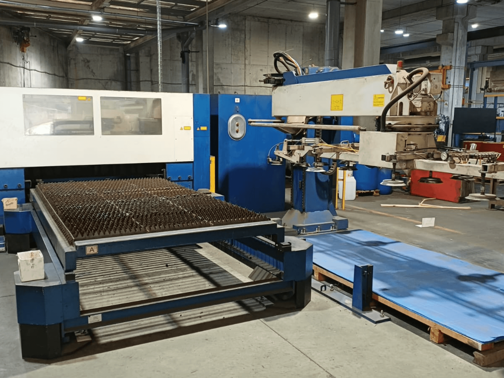 Macchina per il taglio laser a CO₂ TRUMPF TRUMATIC L 3030, vista laterale, che mostra il tavolo di taglio con superficie a punte e il braccio robotico.