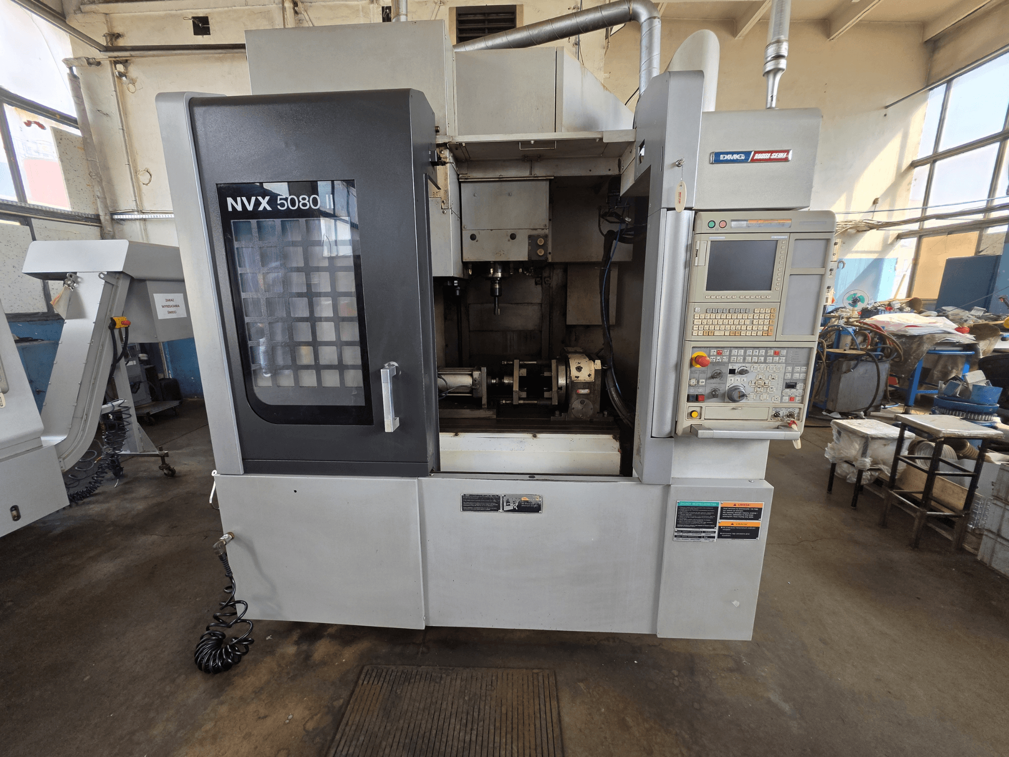 Vista frontale del centro di lavorazione verticale DMG Mori Seiki NVX 5080 II/40 con pannello di controllo e finestra trasparente che mostra l'area di lavorazione.