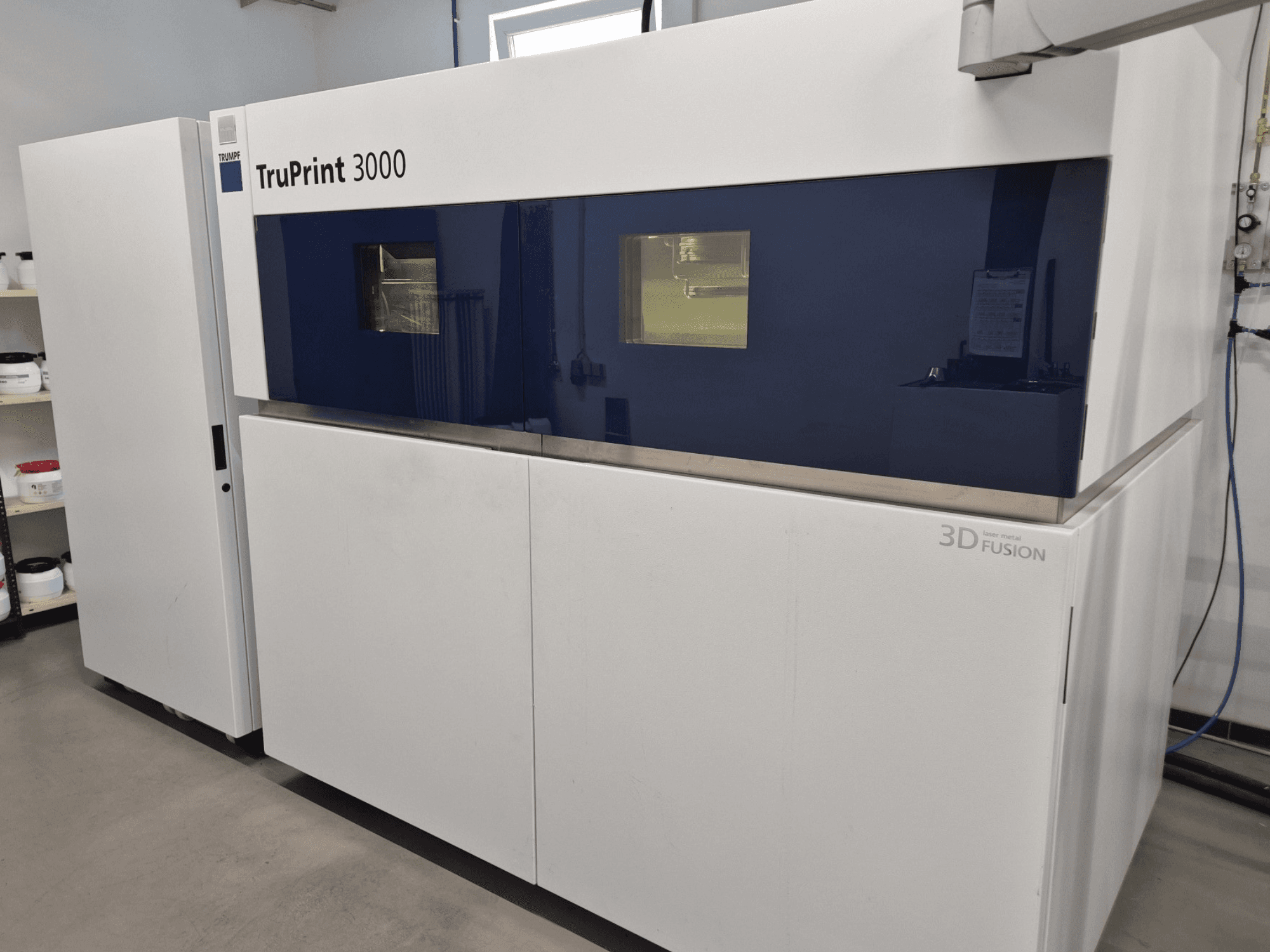 La stampante 3D TruPrint 3000 in metallo in vista frontale, con design a pannelli blu e tecnologia di fusione laser.