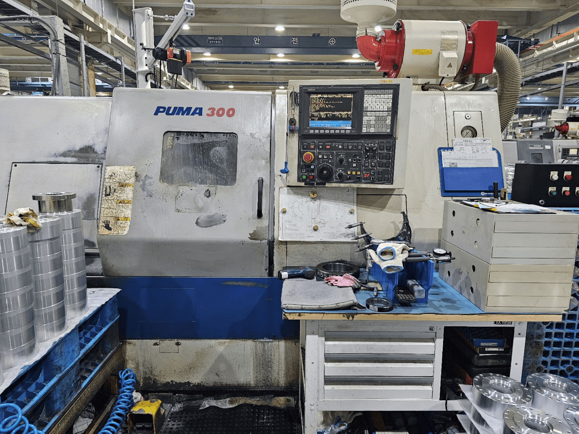 Macchina CNC PUMA 300 in un'officina; vista frontale che mostra il pannello di controllo, gli utensili e le parti metalliche su un banco di lavoro.