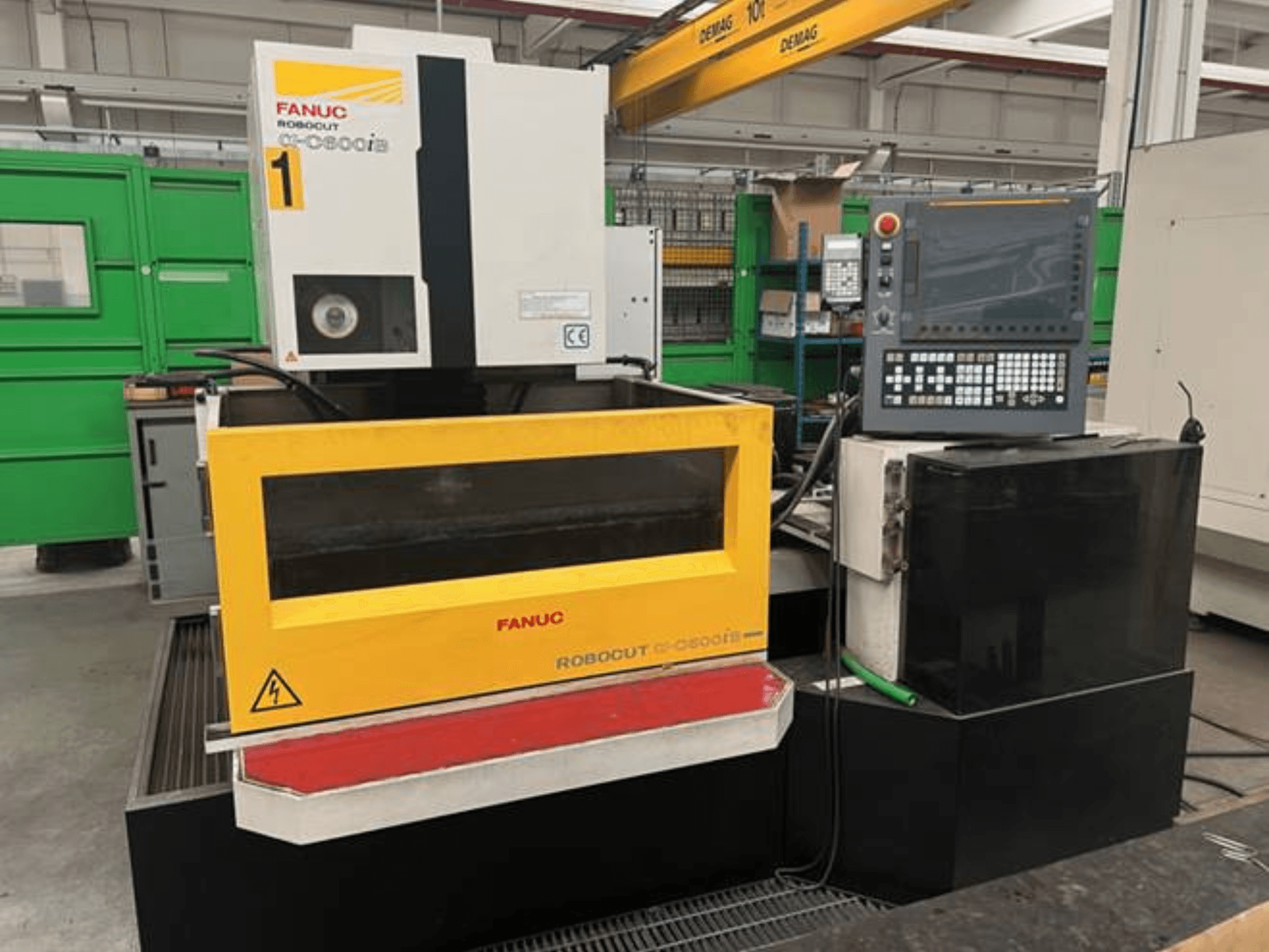 Modello FANUC Robodrill C-0 in vista frontale, con involucro e pannello di controllo gialli, con avvisi di sicurezza visibili.