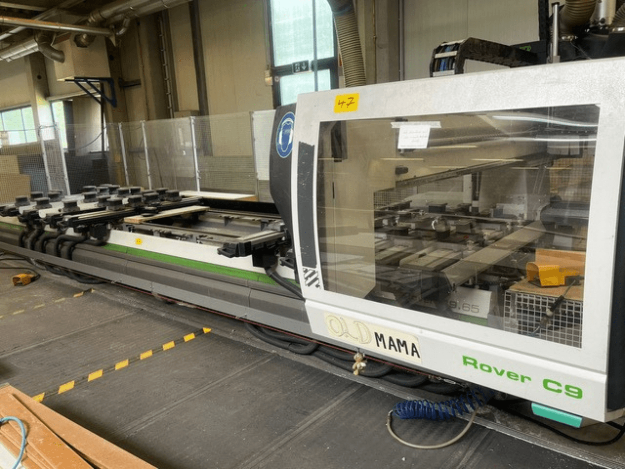 Router CNC BIESSE Rover C 9.65 in un'officina, vista laterale che mostra il pannello di controllo e il piano di lavoro con i morsetti.