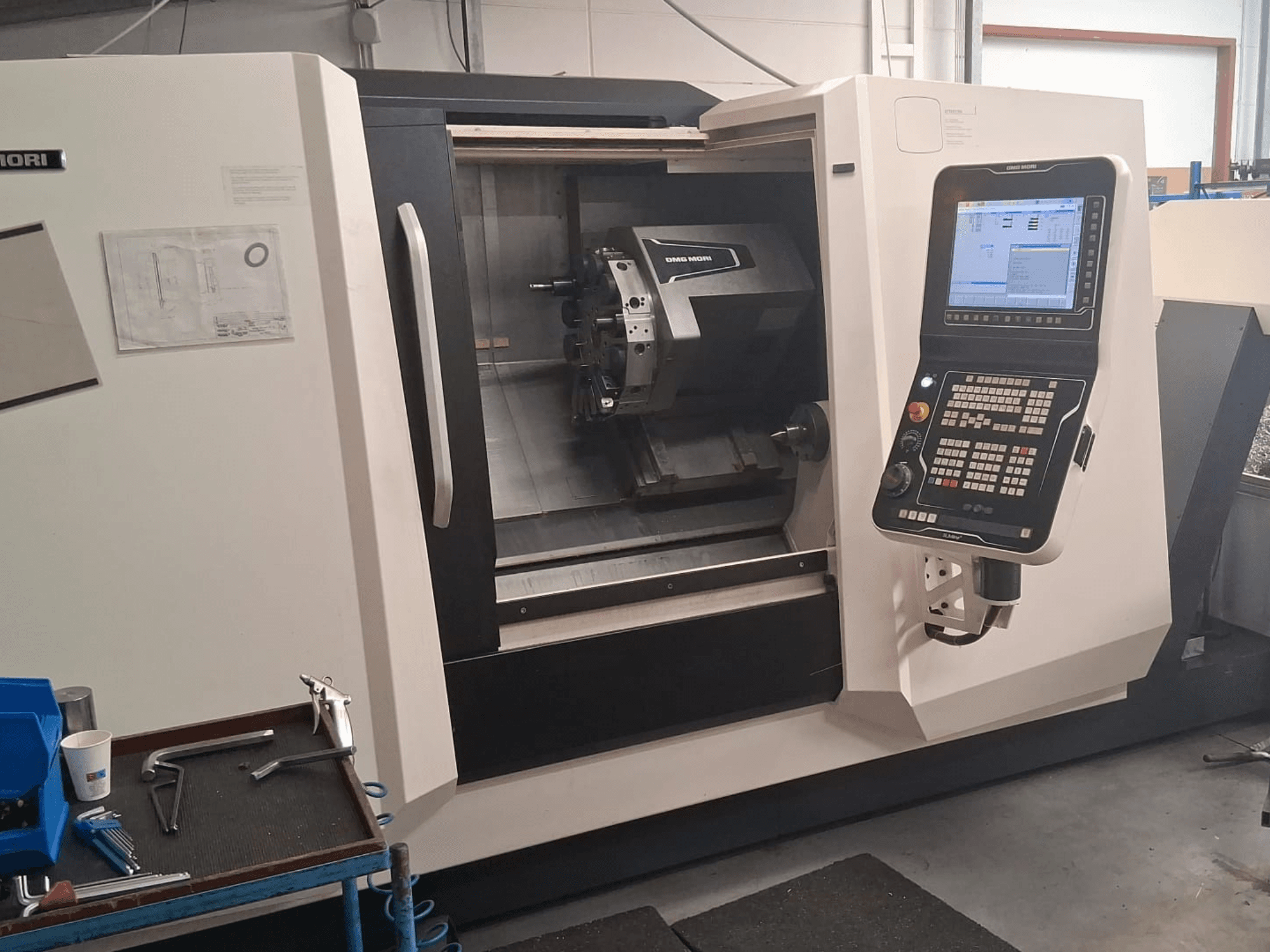 Tornio orizzontale DMG MORI CLX450 in vista frontale, con pannello di controllo e area di lavoro con utensili e documentazione.