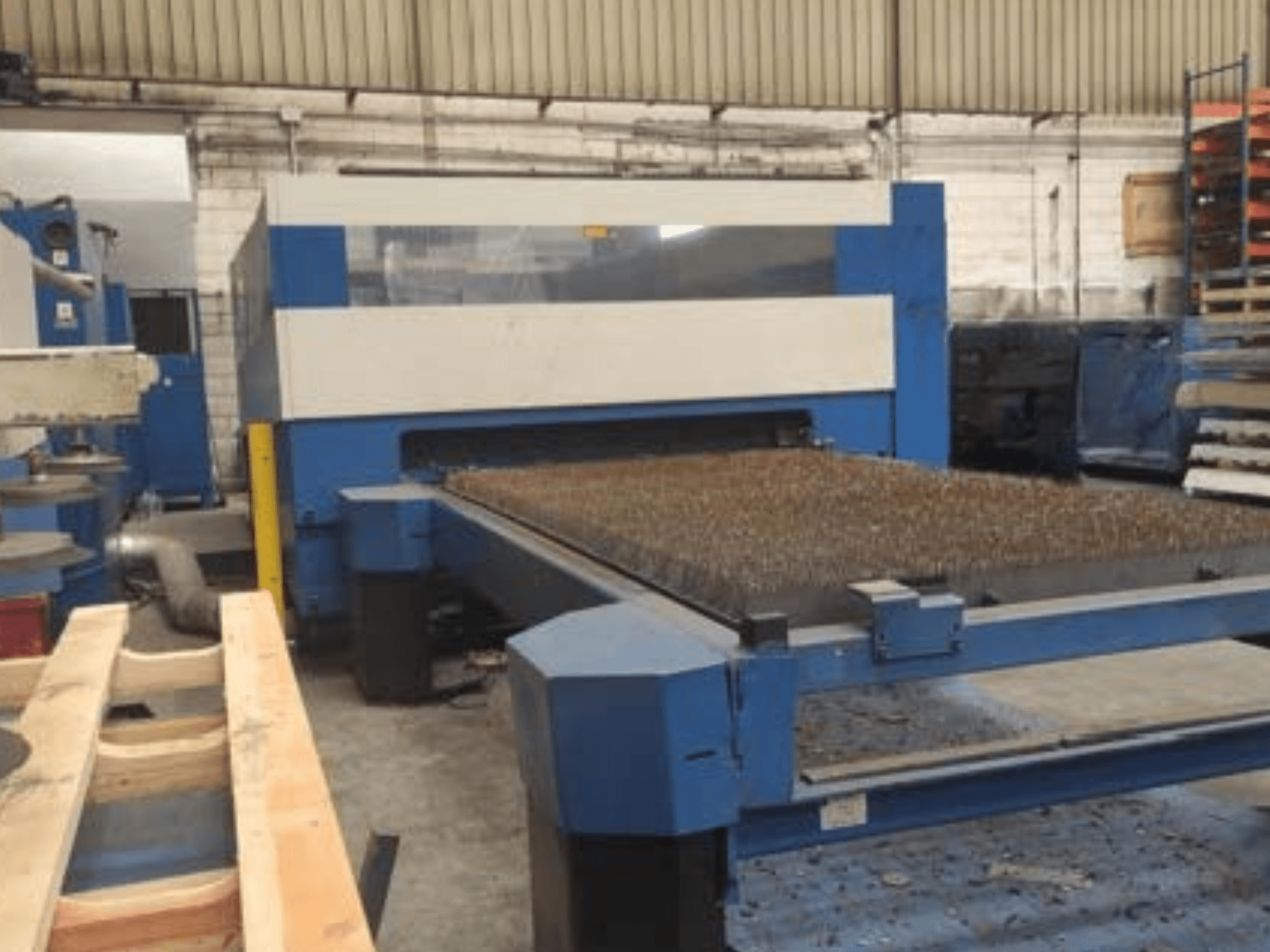 Macchina da taglio laser blu con letto in metallo testurizzato, vista laterale, che mostra la configurazione operativa in uno spazio di lavoro industriale.
