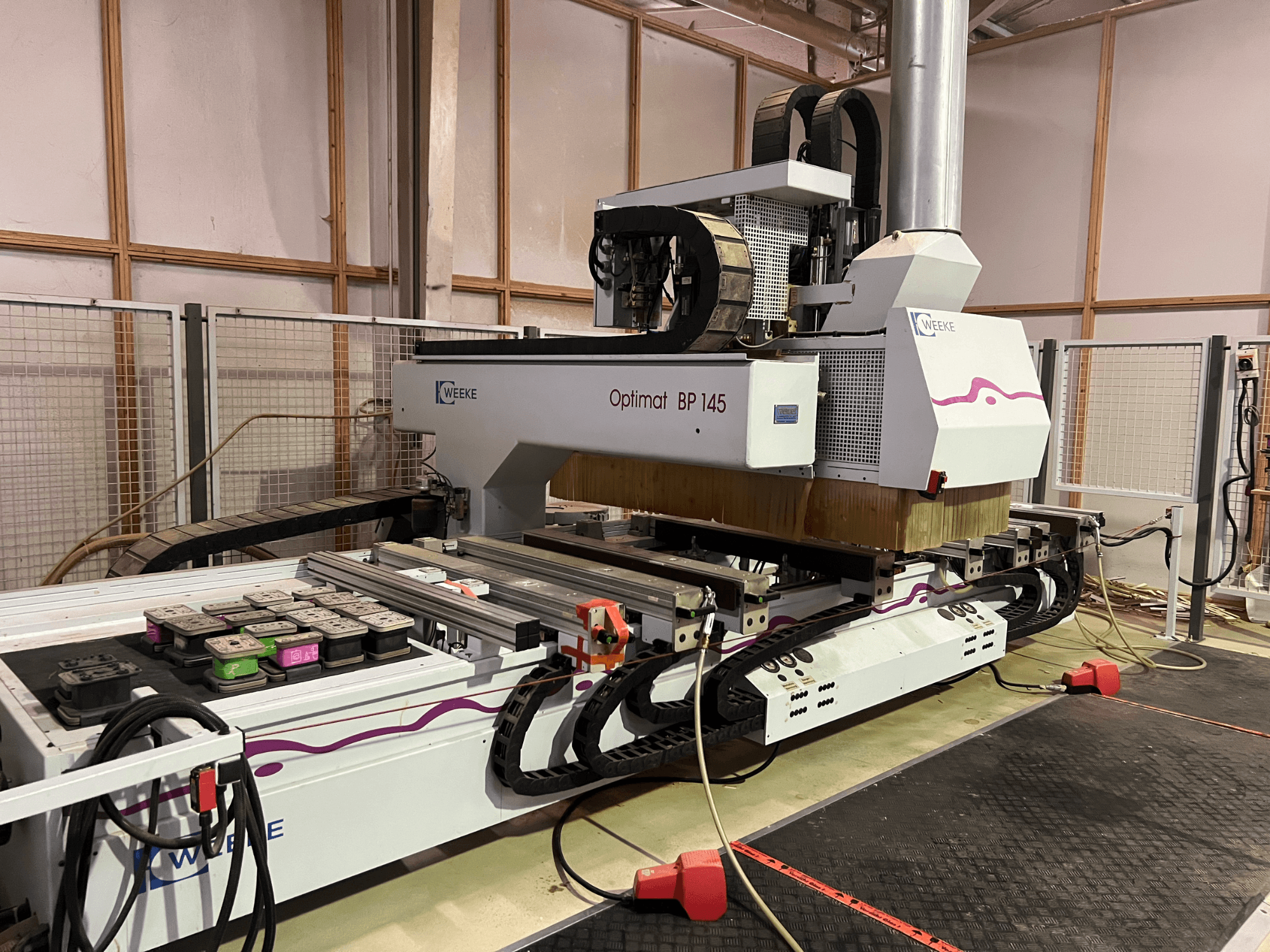 WEEKE Optimat BP 145 in una fabbrica, che mostra una macchina CNC con pulsanti di controllo e cavi, vista di lato.