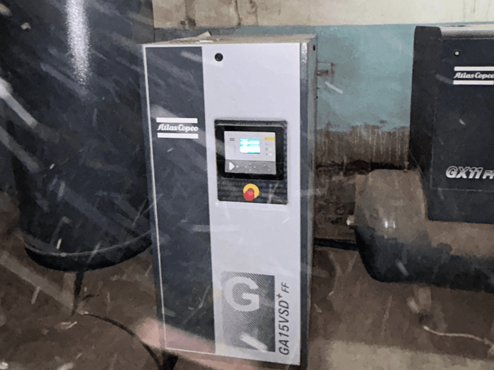 Compressore d'aria Atlas Copco GA15VSD+FF, vista frontale, con pannello di controllo dotato di display e pulsante rosso di arresto di emergenza.