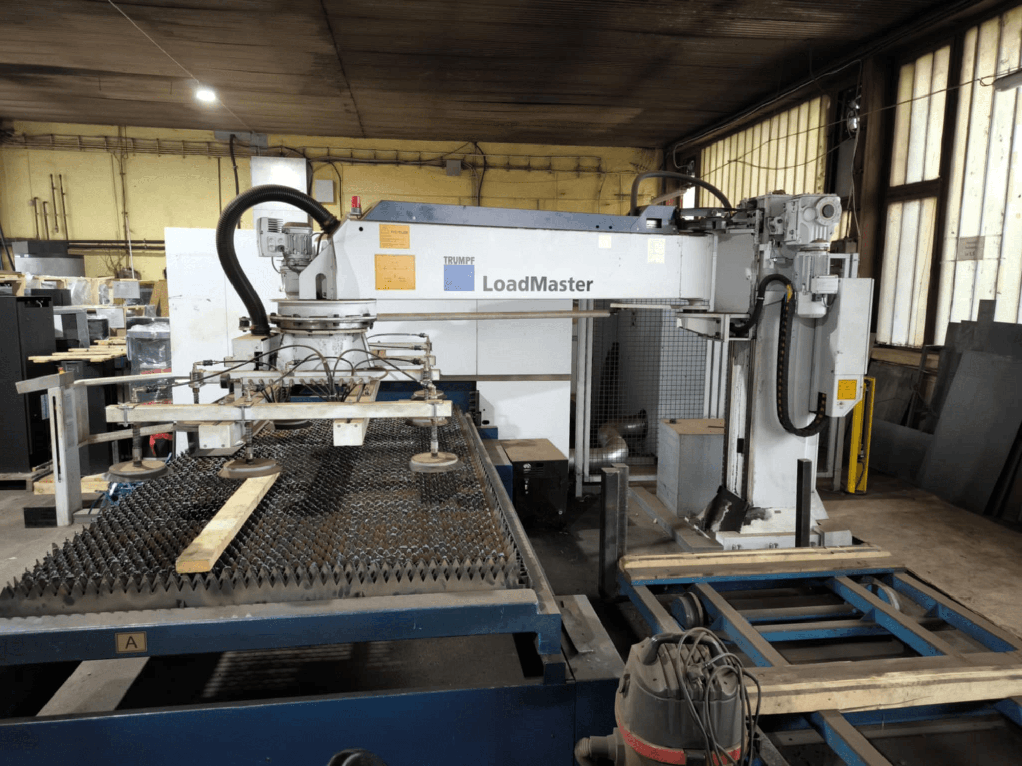 Macchina da taglio TRUMPF TRULASER 3030 FIBER, vista frontale, con sistema LoadMaster e posizionata su un tavolo di lavoro grigliato.
