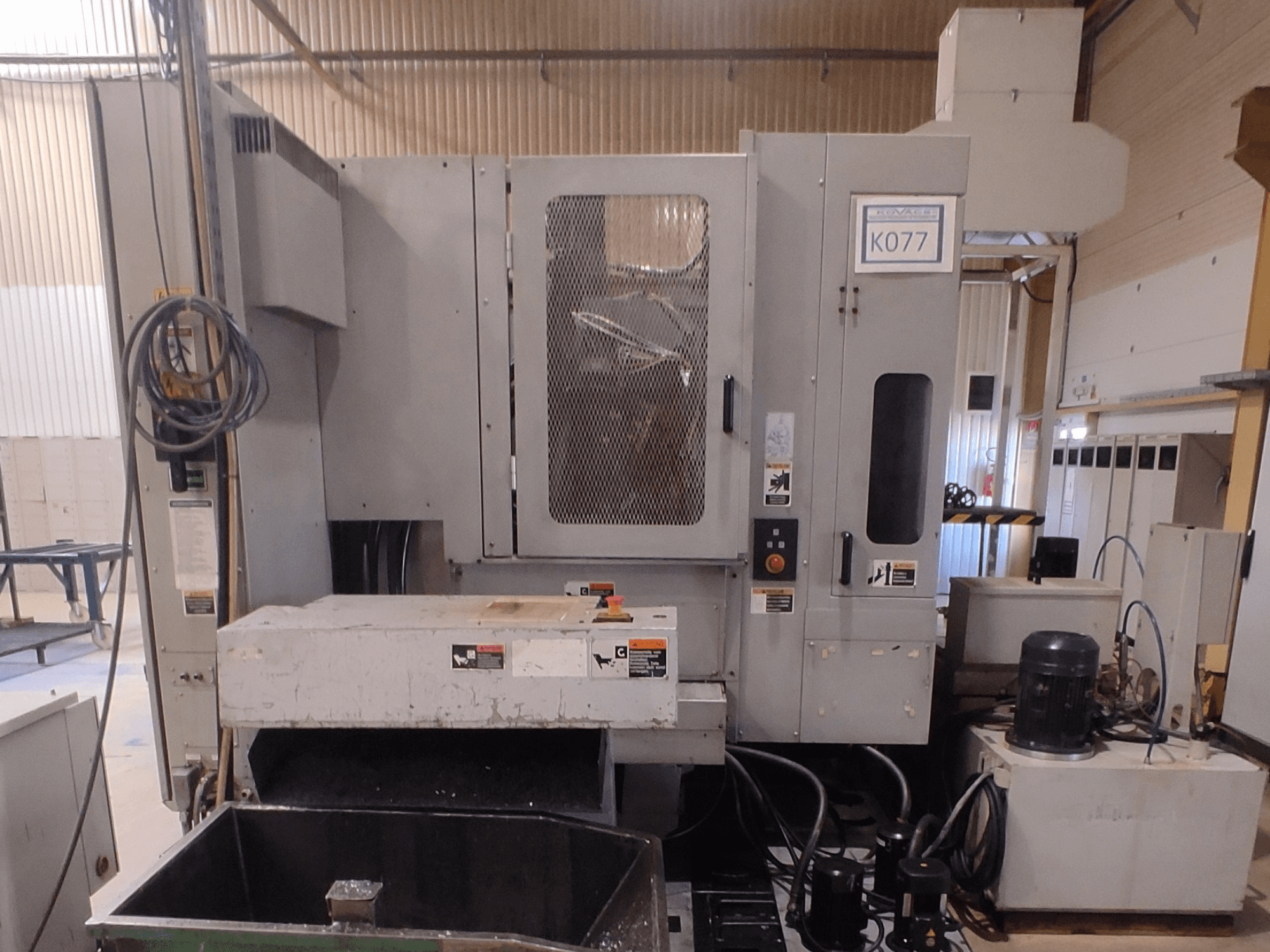 Macchina industriale a controllo numerico grigia con ampio piano di lavoro, vista laterale, con pannello di controllo e serbatoio del refrigerante, modello K077.