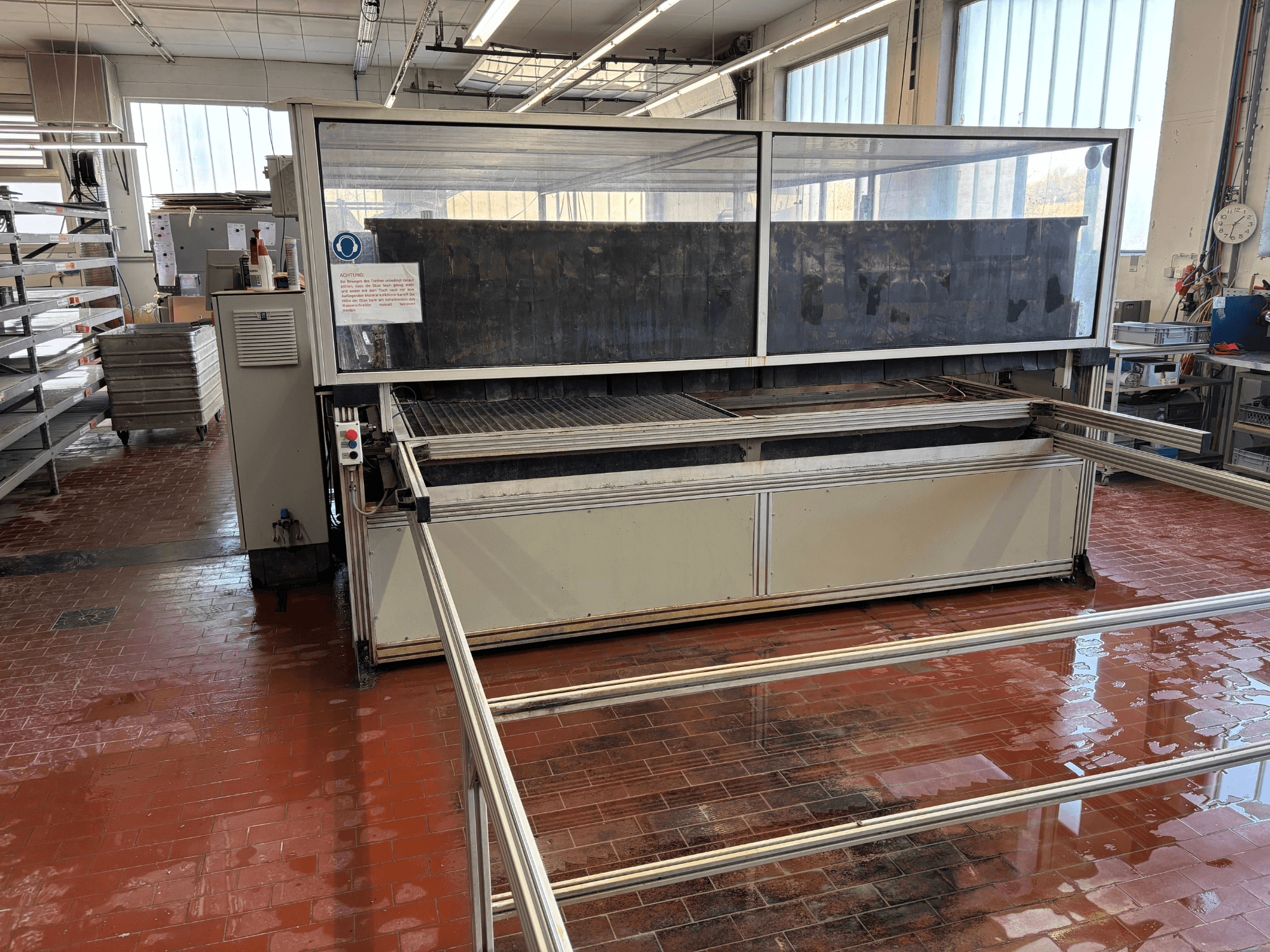 Macchina per il taglio a getto d'acqua EXPERT SYSTEMTECHNIK cutExpert variojet in un'officina, vista frontale, dotata di un ampio coperchio trasparente.