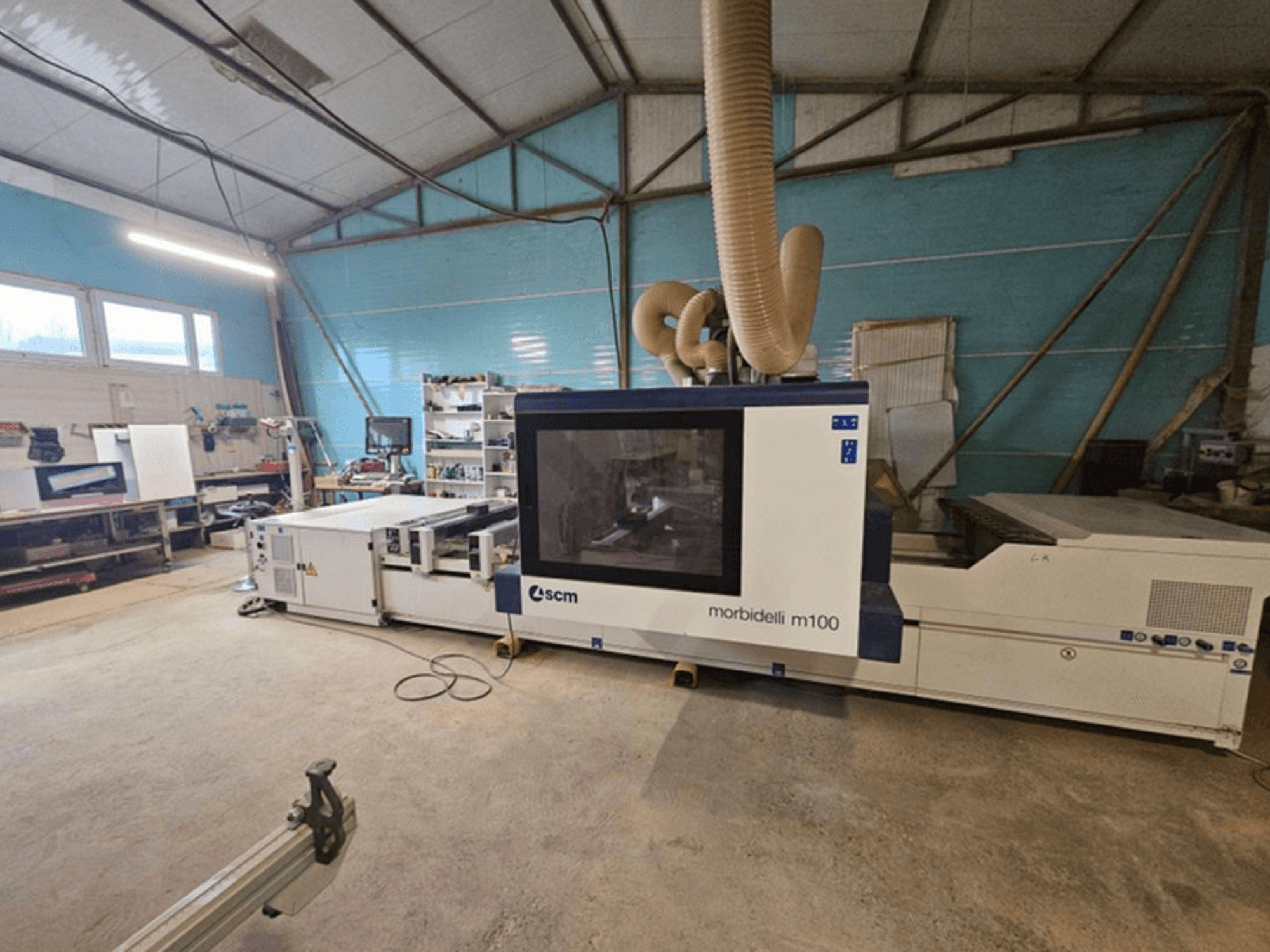 Centro di lavorazione CNC SCM MORBIDELLI M 100 in un'officina, vista frontale con sistema di aspirazione delle polveri e attrezzature che circondano l'area di lavoro.