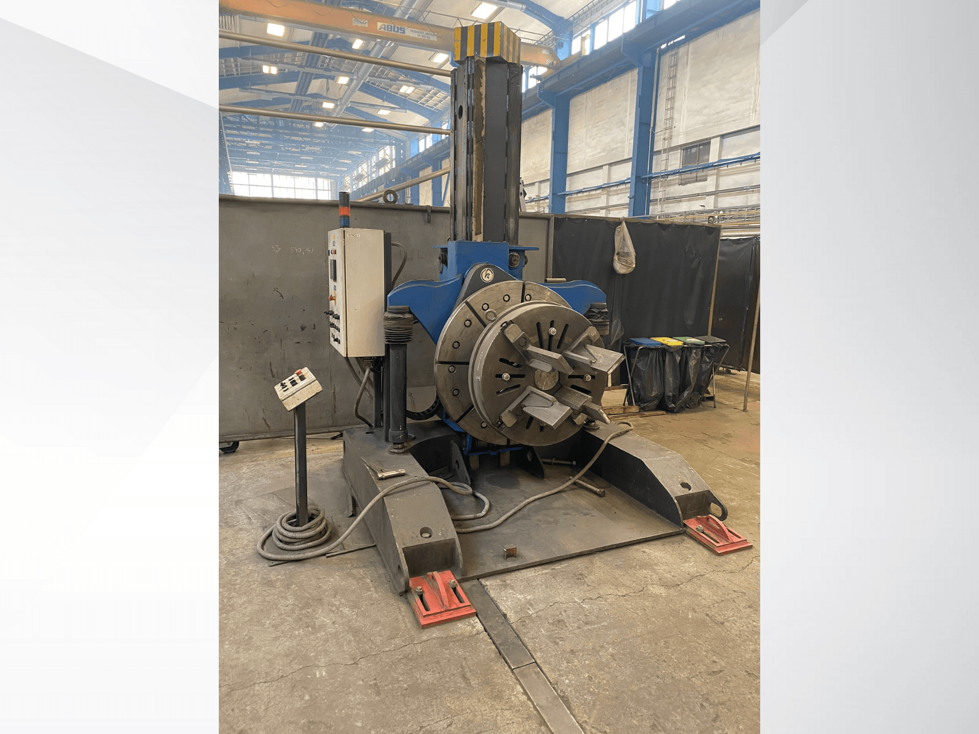 Tornio industriale blu con testa rotante e pannello di controllo, vista laterale, in un'officina.