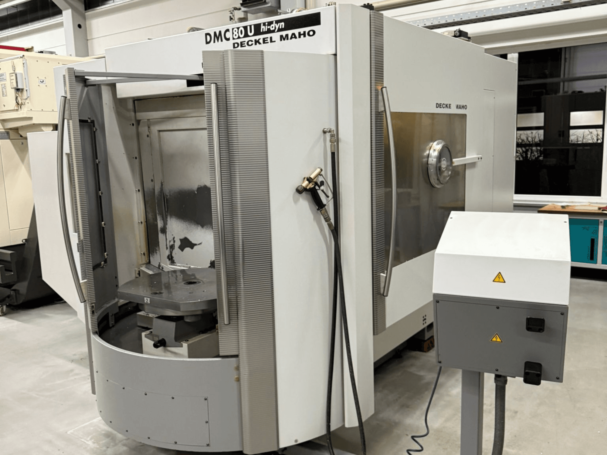 Vista frontale di una fresatrice CNC ad alta velocità Deckel Maho DMC 80 U, con porta di accesso aperta e pannello di controllo laterale.