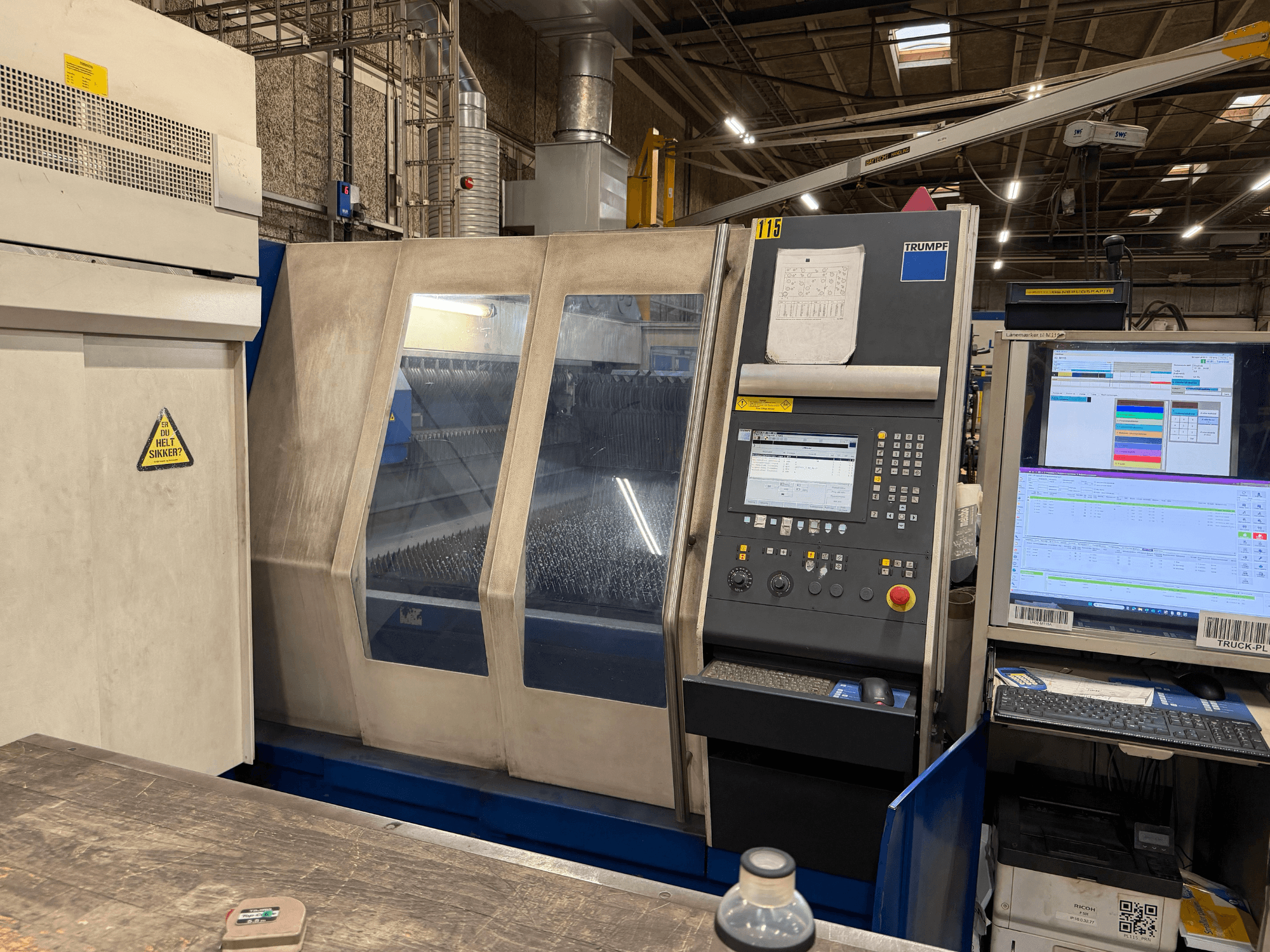 Vista frontale di una macchina laser industriale Trumpf con pannello di controllo e display digitali, ambientata in uno stabilimento.