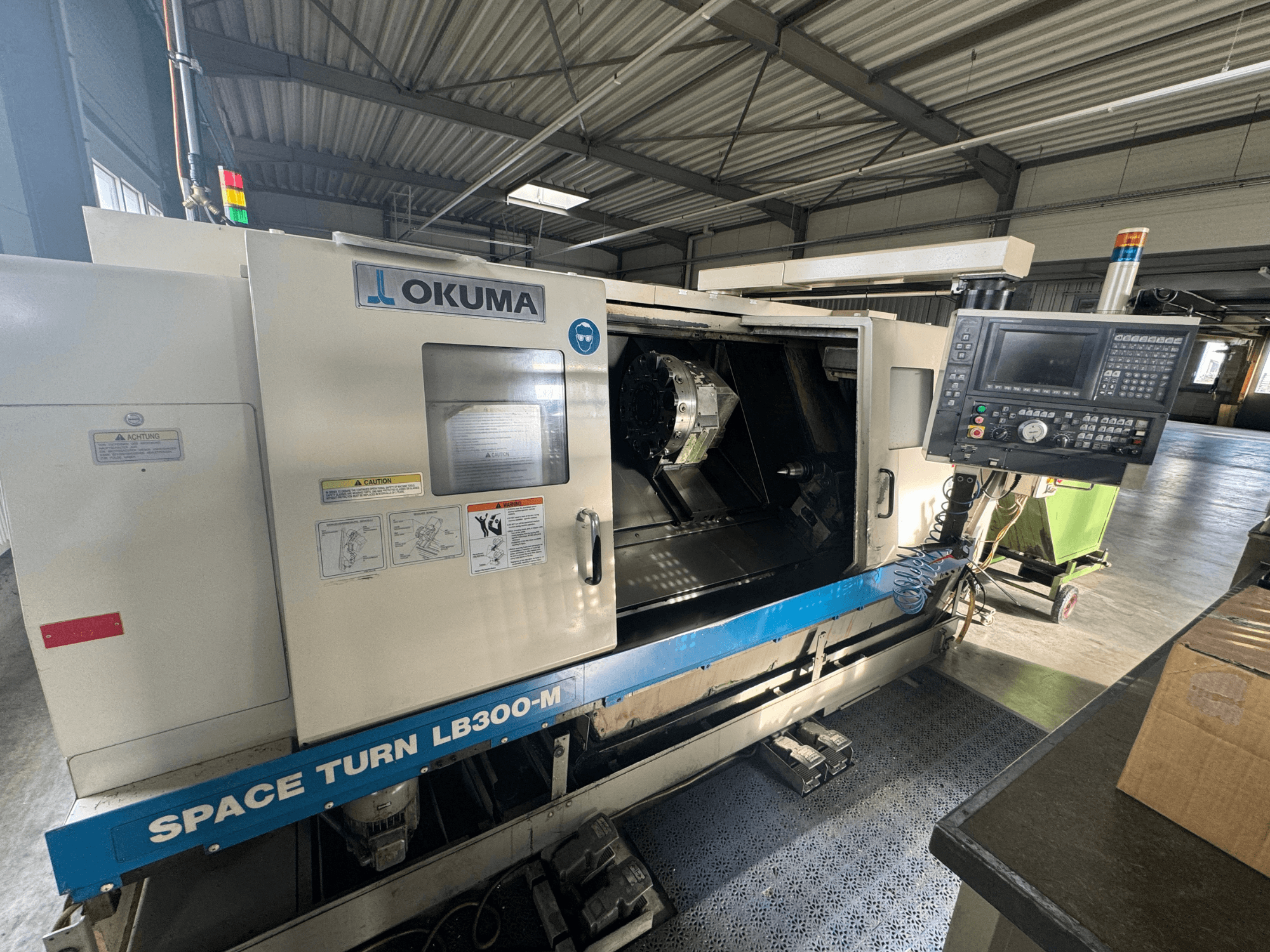 Tornio CNC Okuma Space Turn LB300-M in vista frontale, con pannello di controllo e porta aperta che rivela l'area di lavorazione interna.