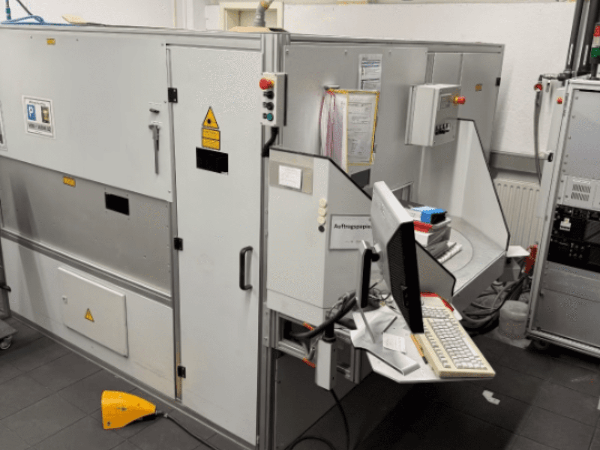 Macchina industriale con terminale informatico, vista laterale; include pulsanti di controllo e segnali di sicurezza.