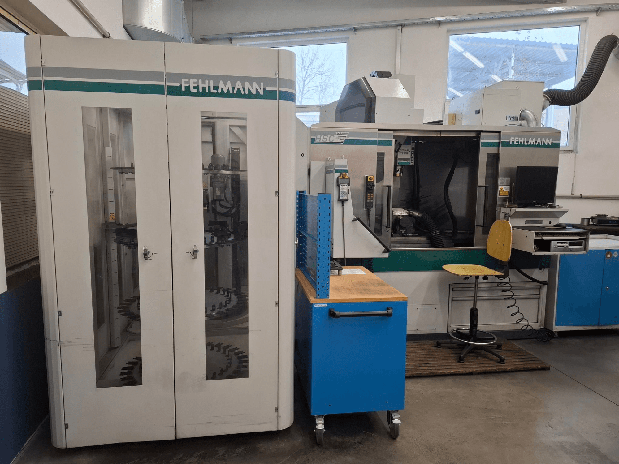 Centro di lavoro FEHLMANN HSC in un'officina; vista frontale con comandi, sedute e magazzino utensili visibili.
