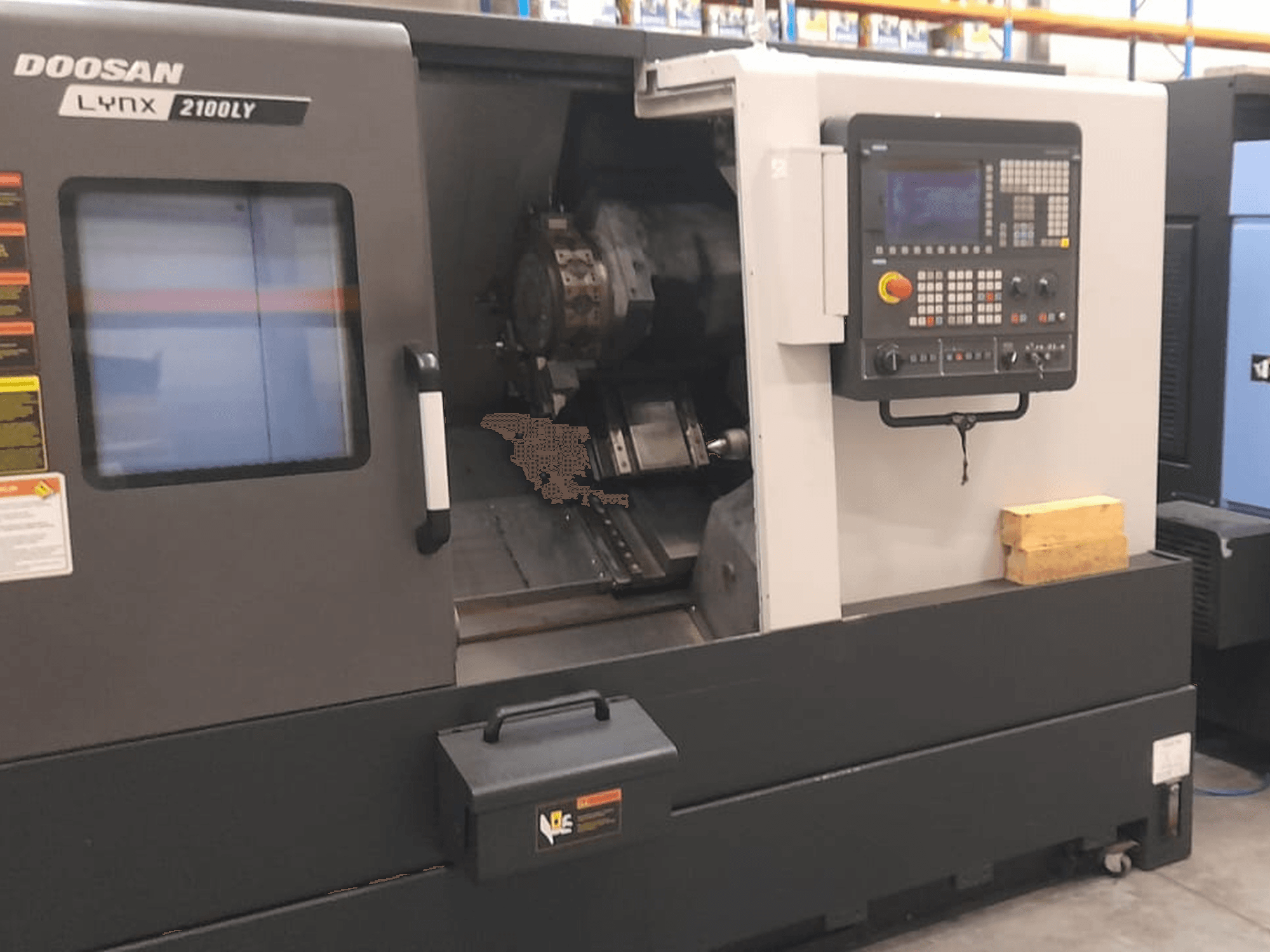 Tornio CNC Doosan Lynx 2100LY, vista frontale che mostra il pannello di controllo, il portautensili e l'area di lavoro interna; etichette tecniche visibili.