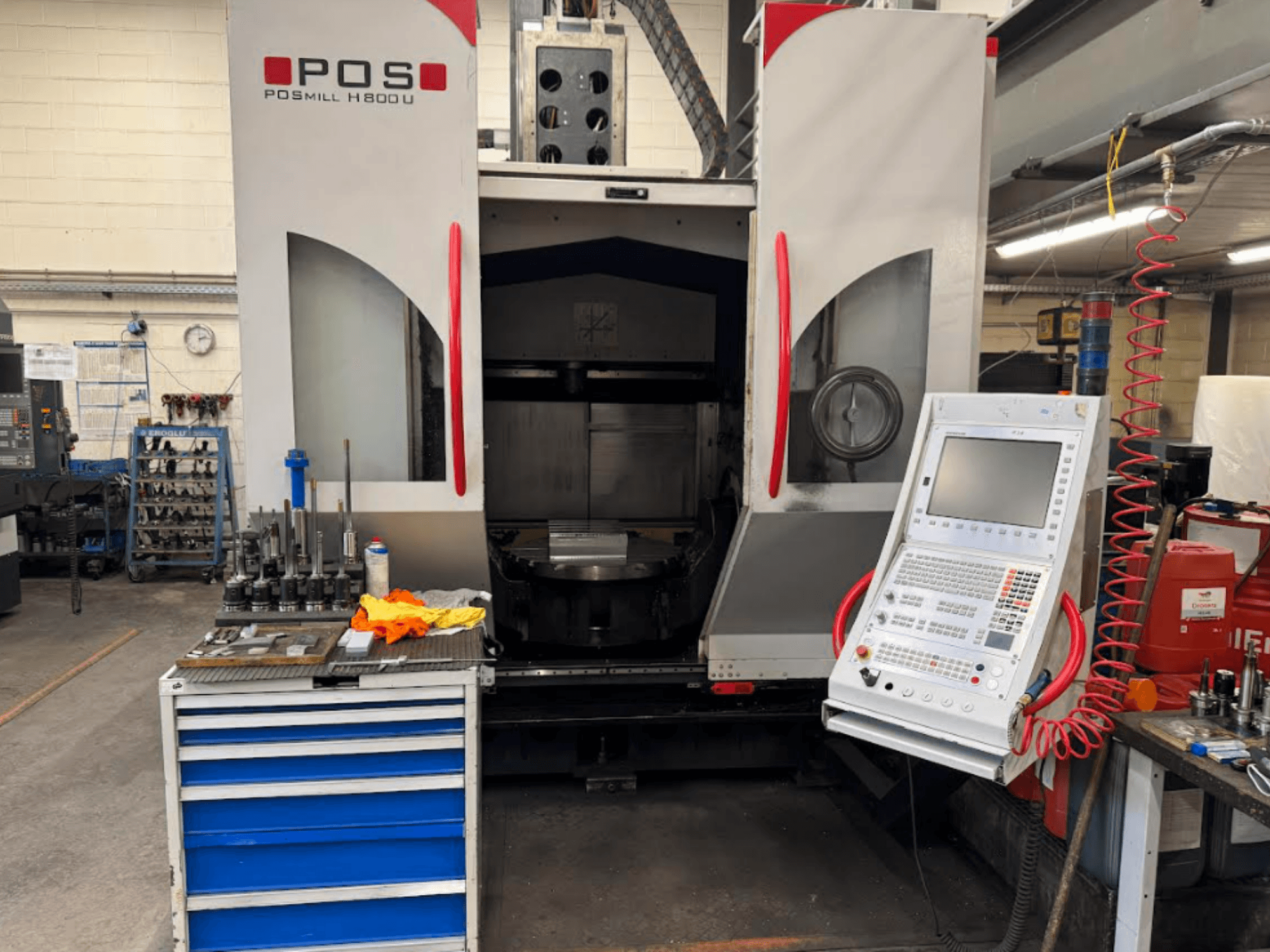 La macchina CNC POSMILL H800 U vista frontalmente, con il pannello di controllo e l'area di lavoro con utensili e attrezzature nelle vicinanze.