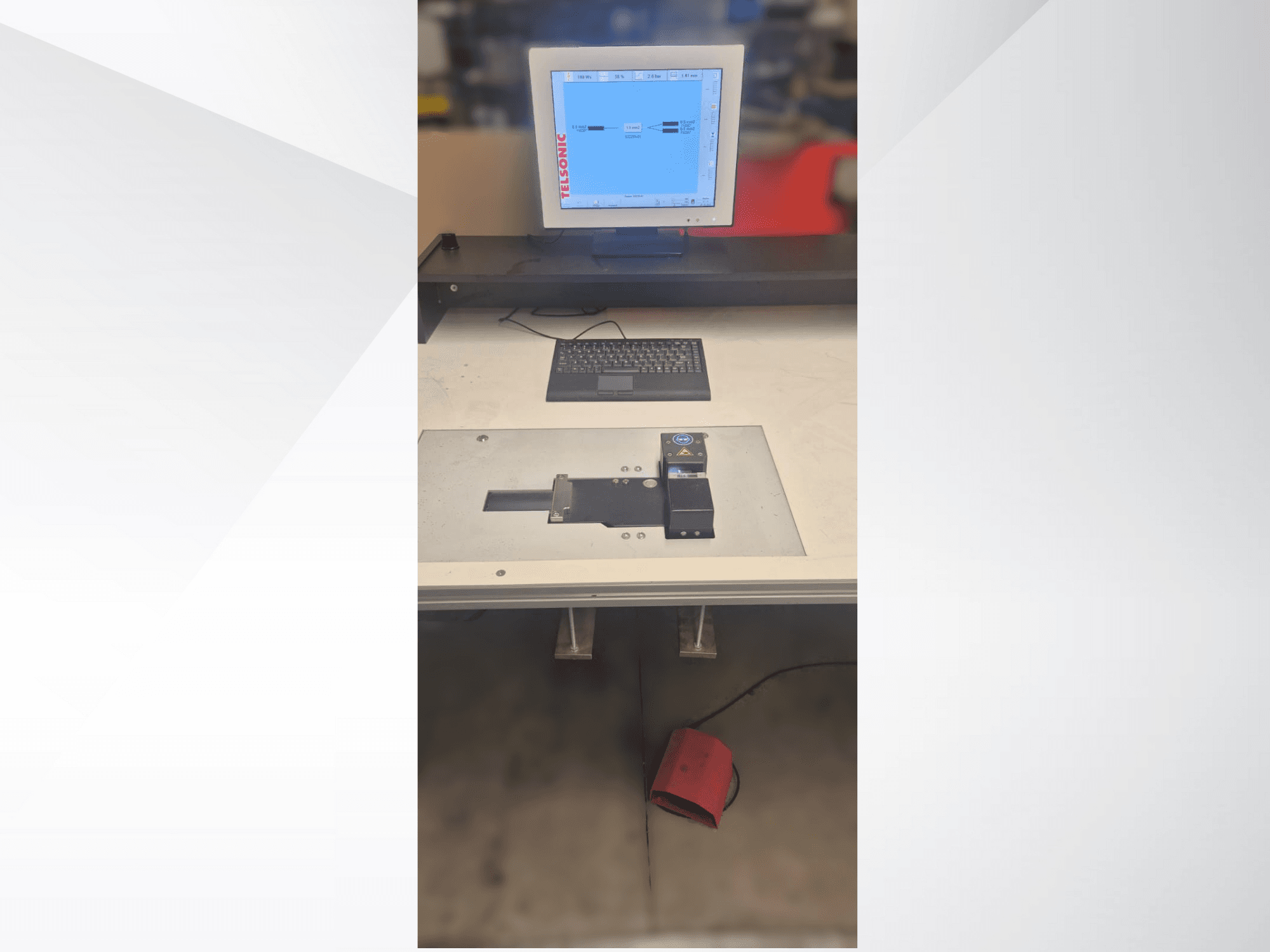 Vista dall'alto di una stazione di test con monitor di computer, tastiera e pannello di controllo con un pulsante e una luce verde.