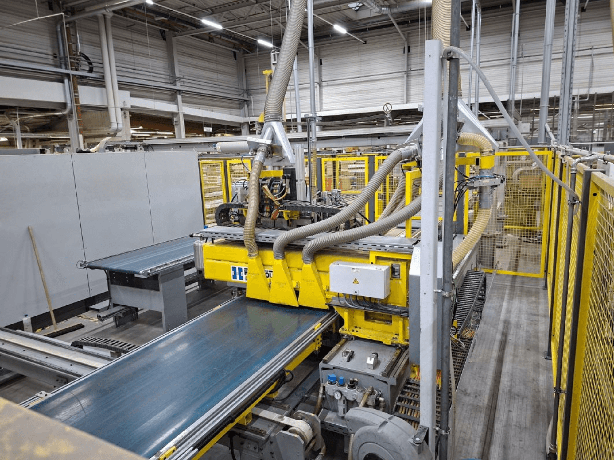 Sistema di trasporto industriale visto lateralmente, con macchinari gialli, pannello di controllo e attacchi per tubi flessibili per la produzione.