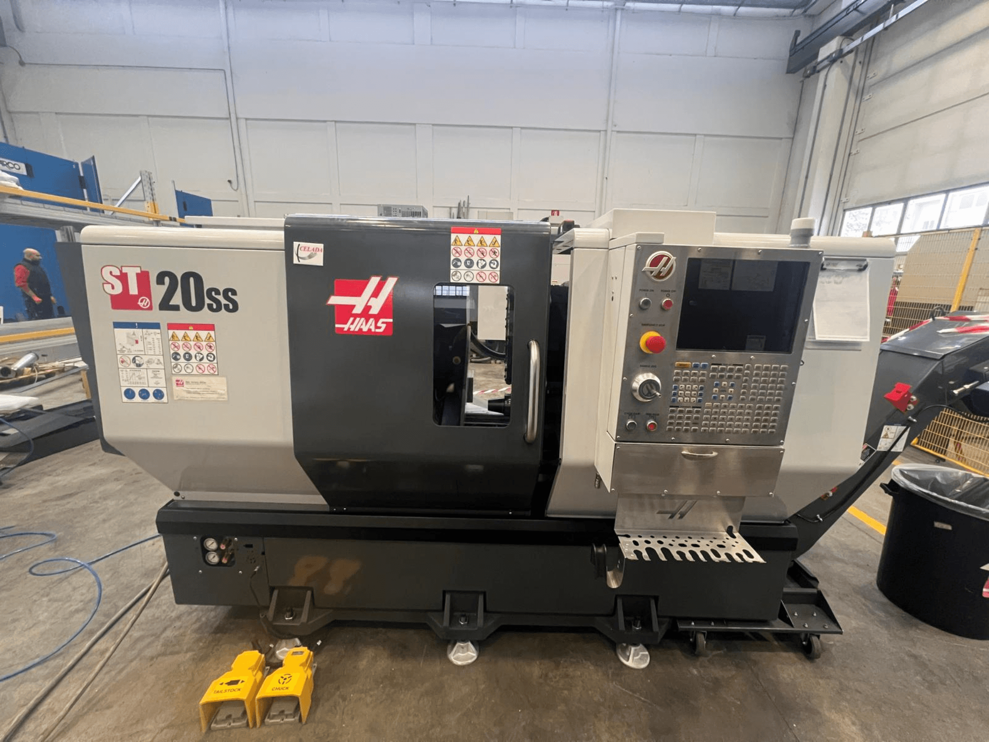 Tornio CNC Haas ST 20SS in vista laterale, con pannello di controllo, etichette di sicurezza e pedali sul pavimento.