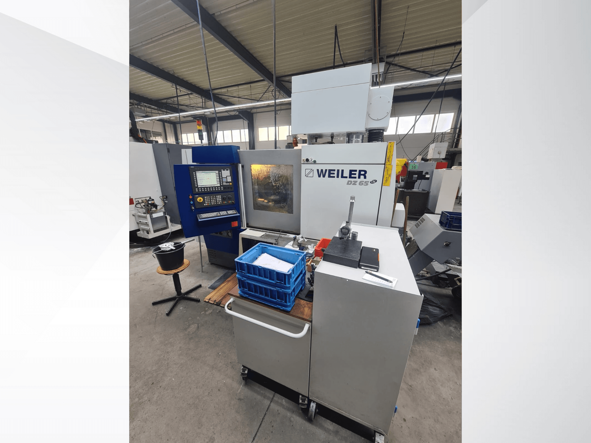 Macchina CNC Weiler DZ 65 in un'officina, vista frontale con pannello di controllo, utensili e contenitori blu visibili.