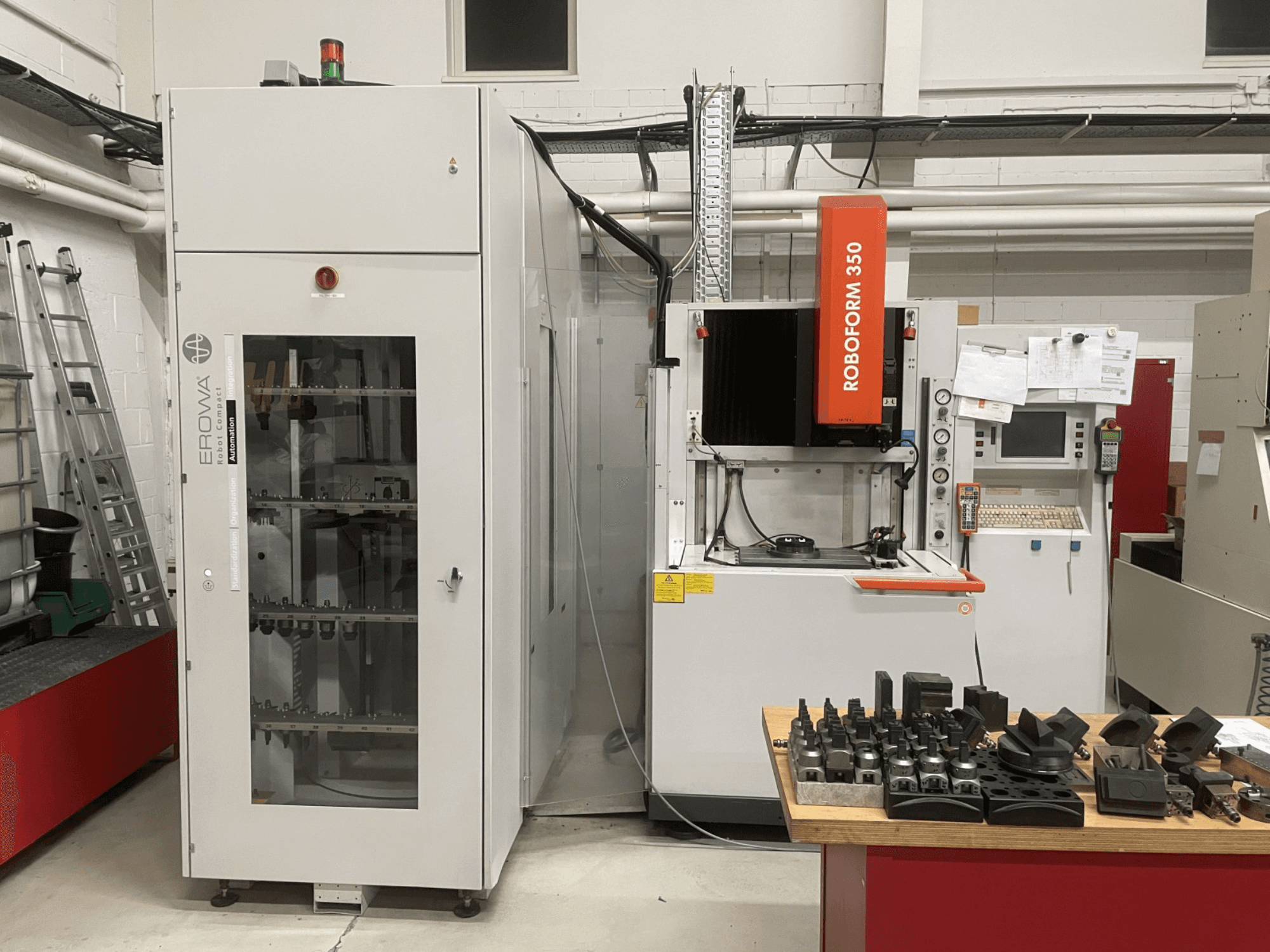 Macchina per elettroerosione a tuffo CHARMILLES Roboform 350, vista frontale, con utensili esposti su un tavolo e attrezzature adiacenti.