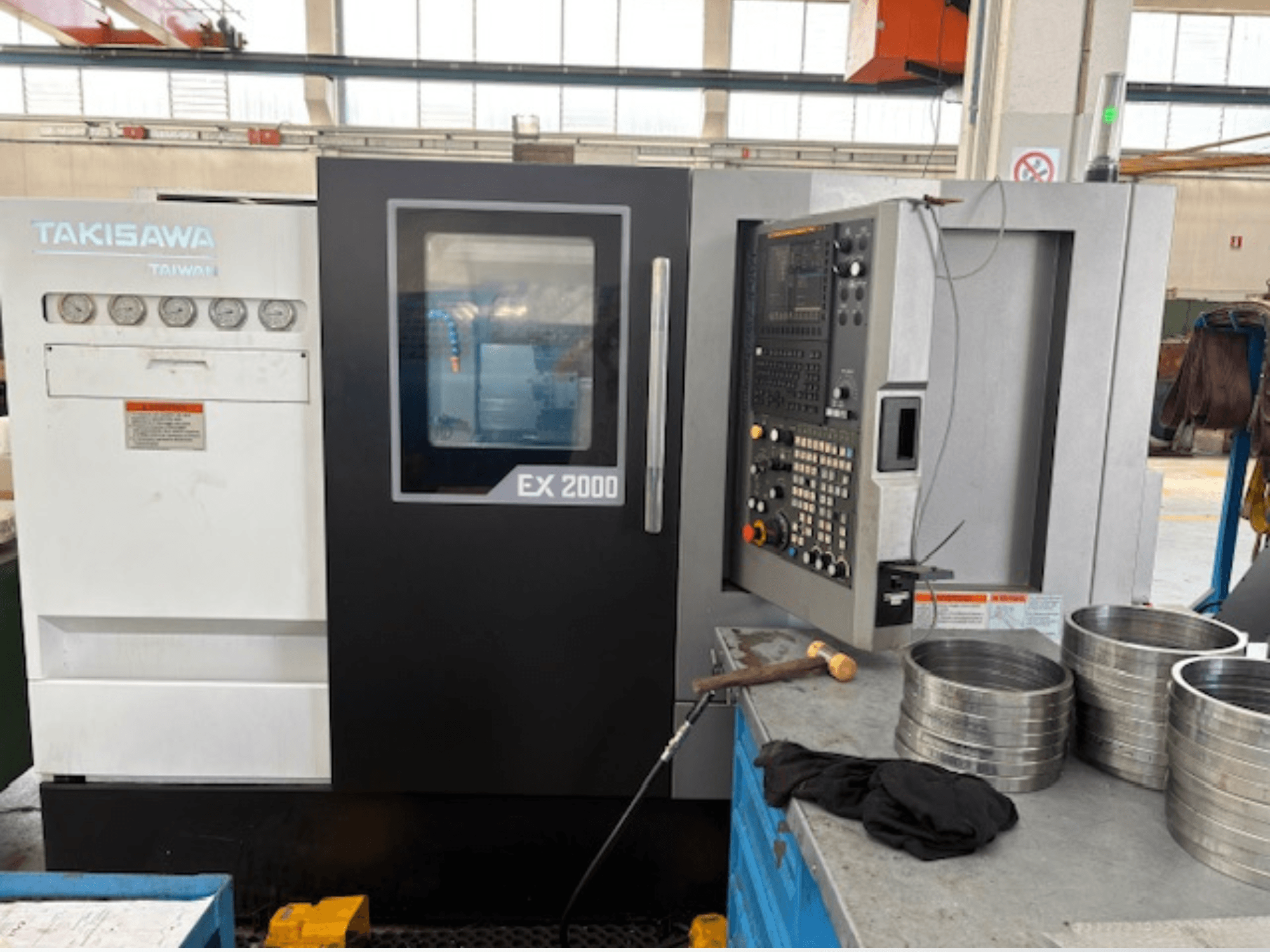 Macchina CNC Takisawa EX 2000, vista frontale, con pannello di controllo, indicatori e parti metalliche su un tavolo da officina.