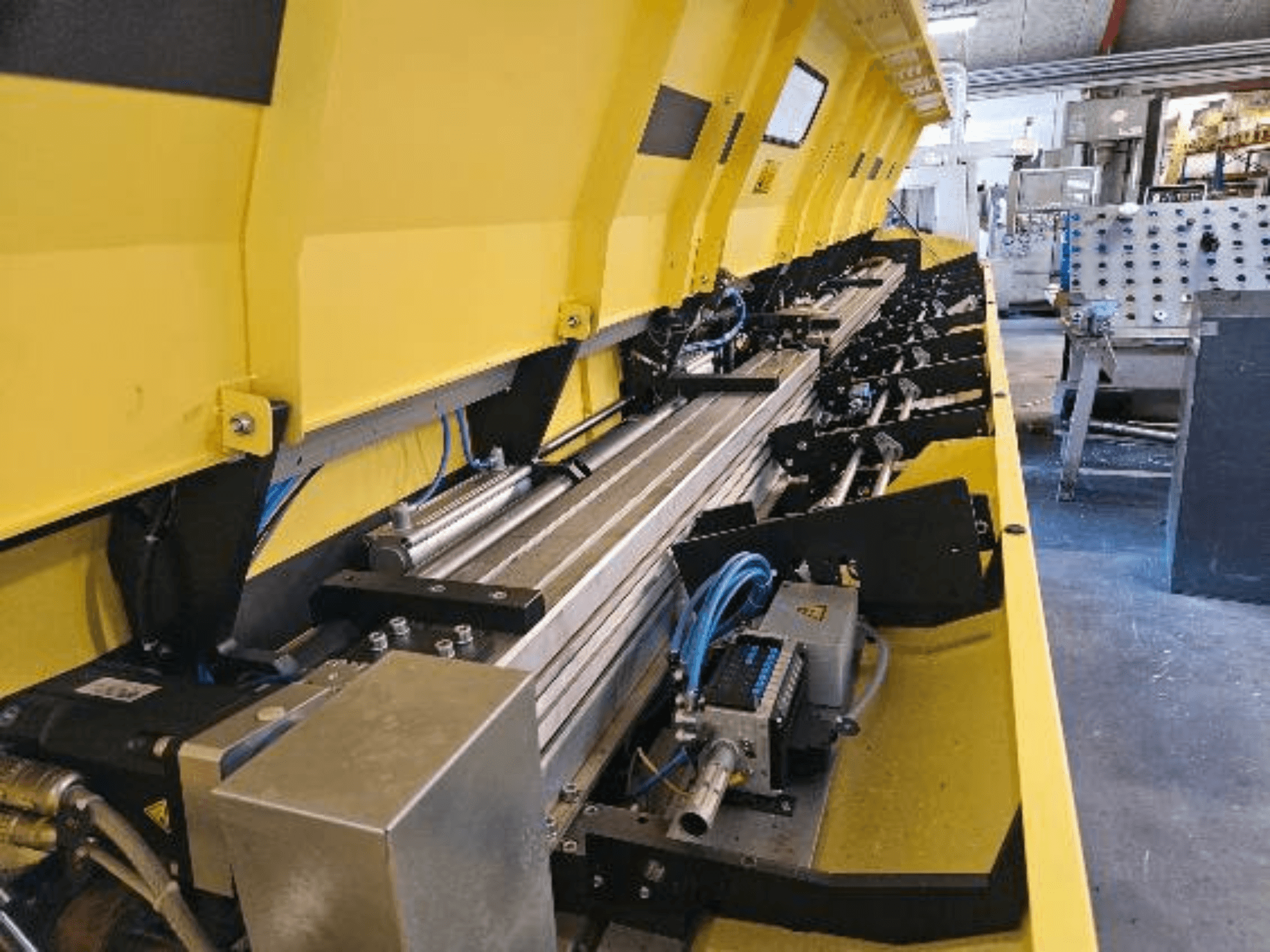 Vista ravvicinata di una macchina idraulica gialla con componenti metallici e binari di trasporto, con tubi e parti elettroniche.