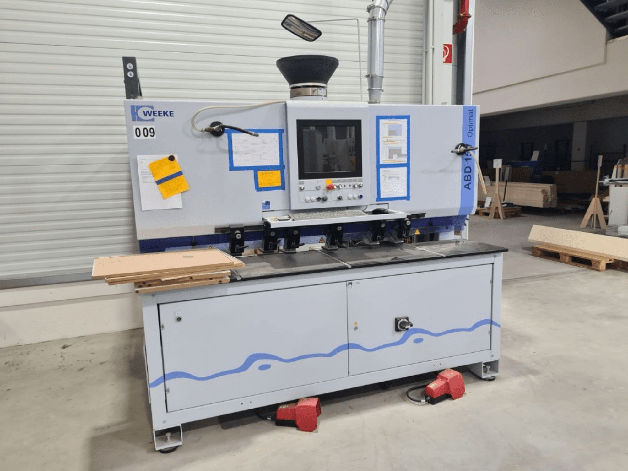 Foratrice multimandrino HOMAG WEEKE OPTIMAT ABD150, vista frontale, con comandi e pannelli di legno impilati.