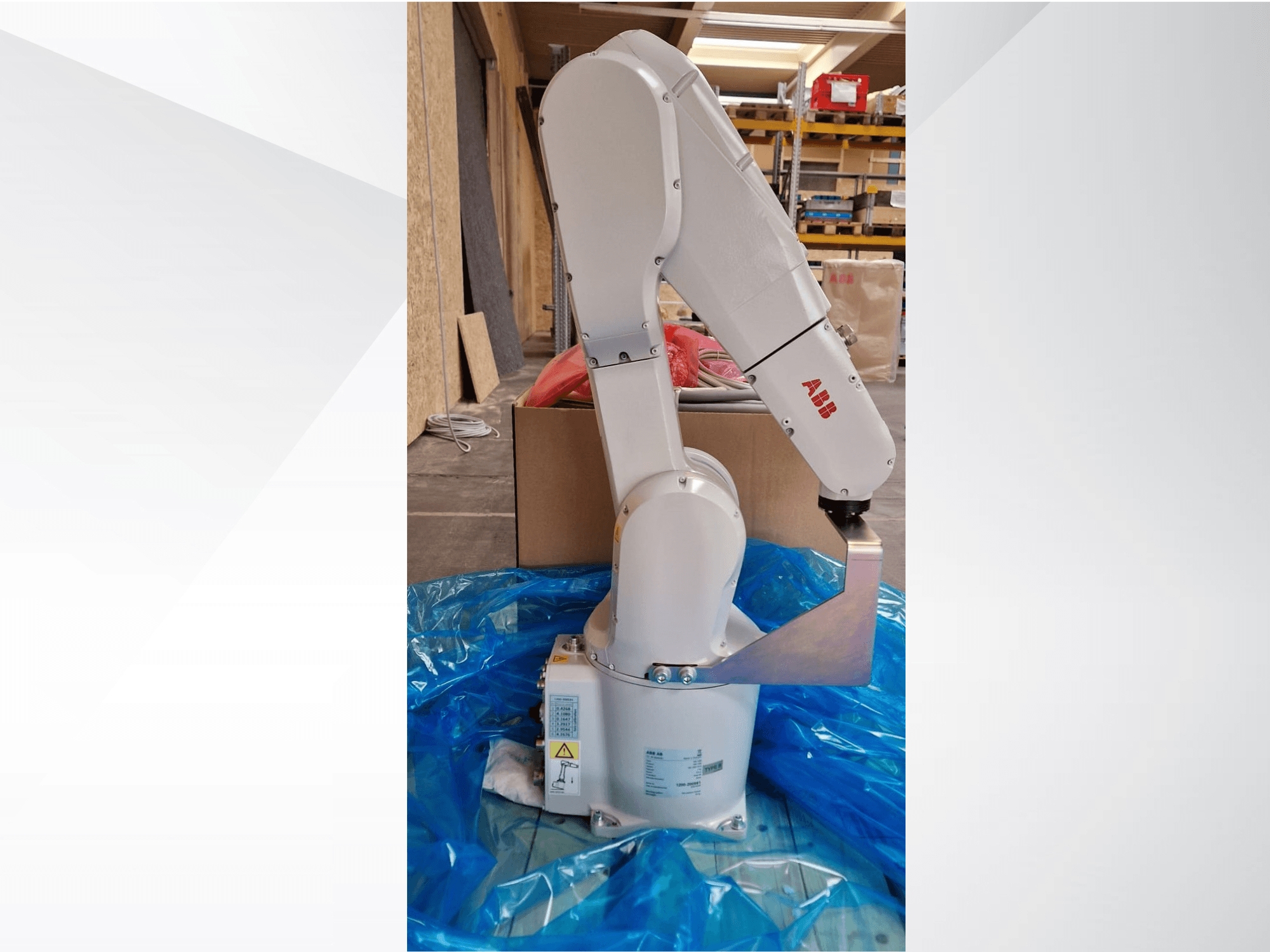Modello di braccio robotico ABB, vista laterale su telo blu, che mostra i giunti articolati e l'effettore finale in metallo, con etichette tecniche visibili.
