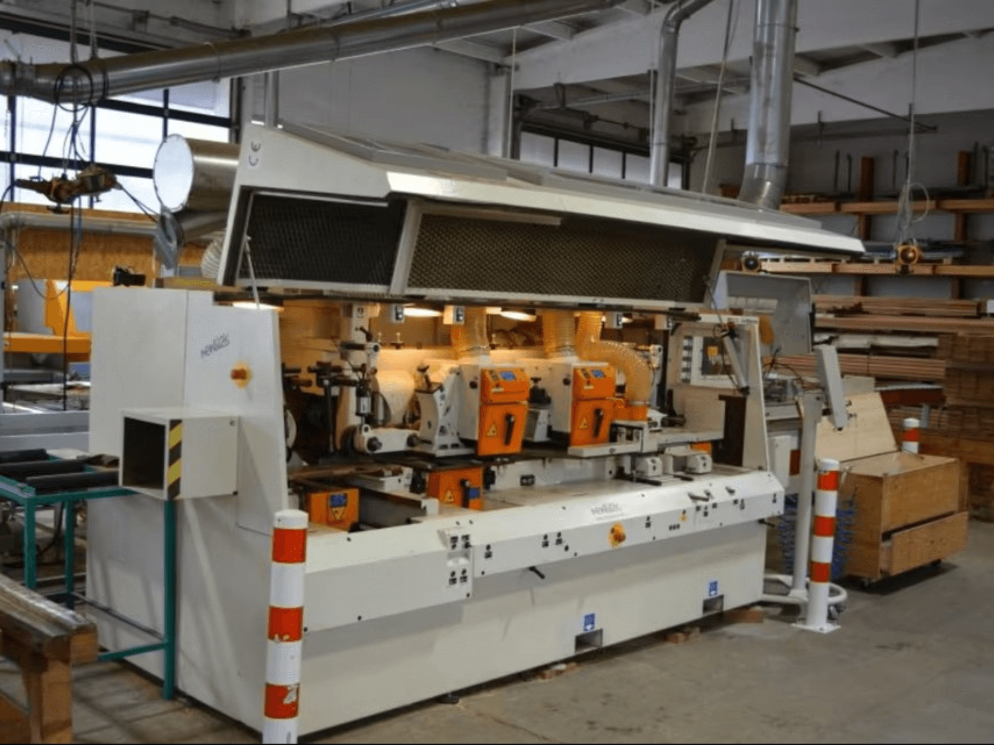 Macchina per la lavorazione del legno PENIGAS, vista frontale, con doppia testa di taglio arancione e sistema di aspirazione della polvere in un'officina.