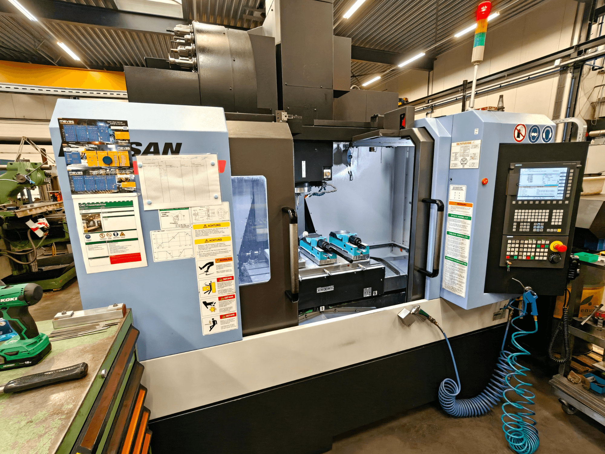Centro di lavoro verticale DOOSAN DNM 400 II in un'officina, con comandi, portautensili e segnaletica di sicurezza, vista frontale.