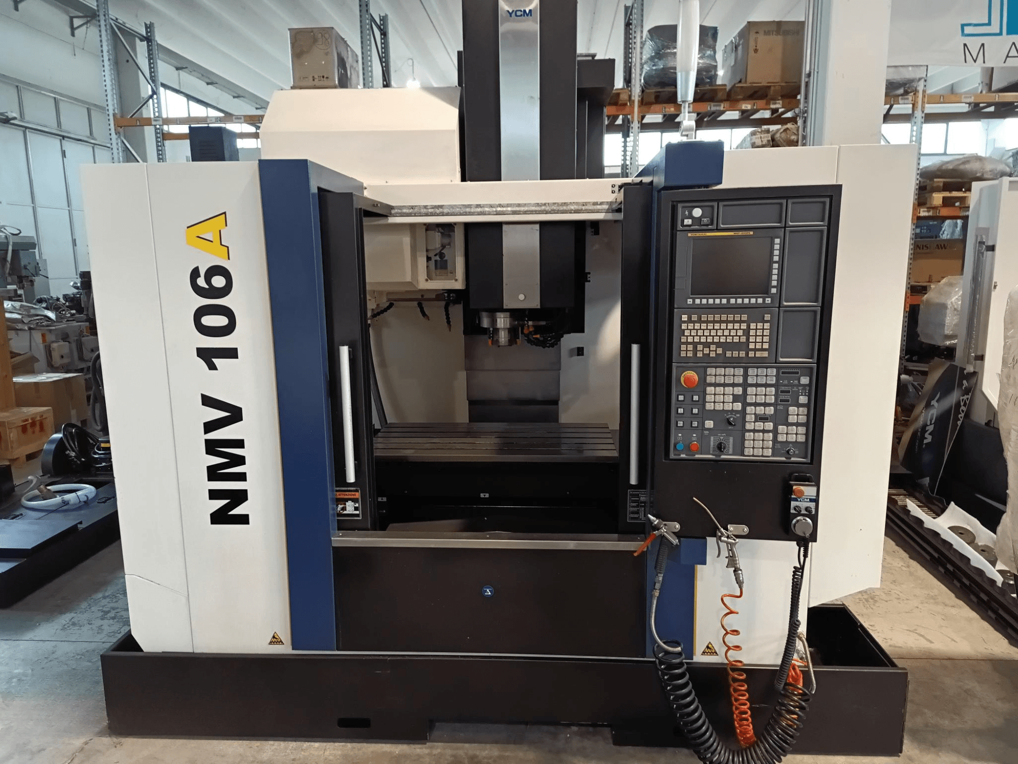 Centro di lavoro YCM NMV 106A, vista frontale, con pannello di controllo con pulsanti e tubi del refrigerante.