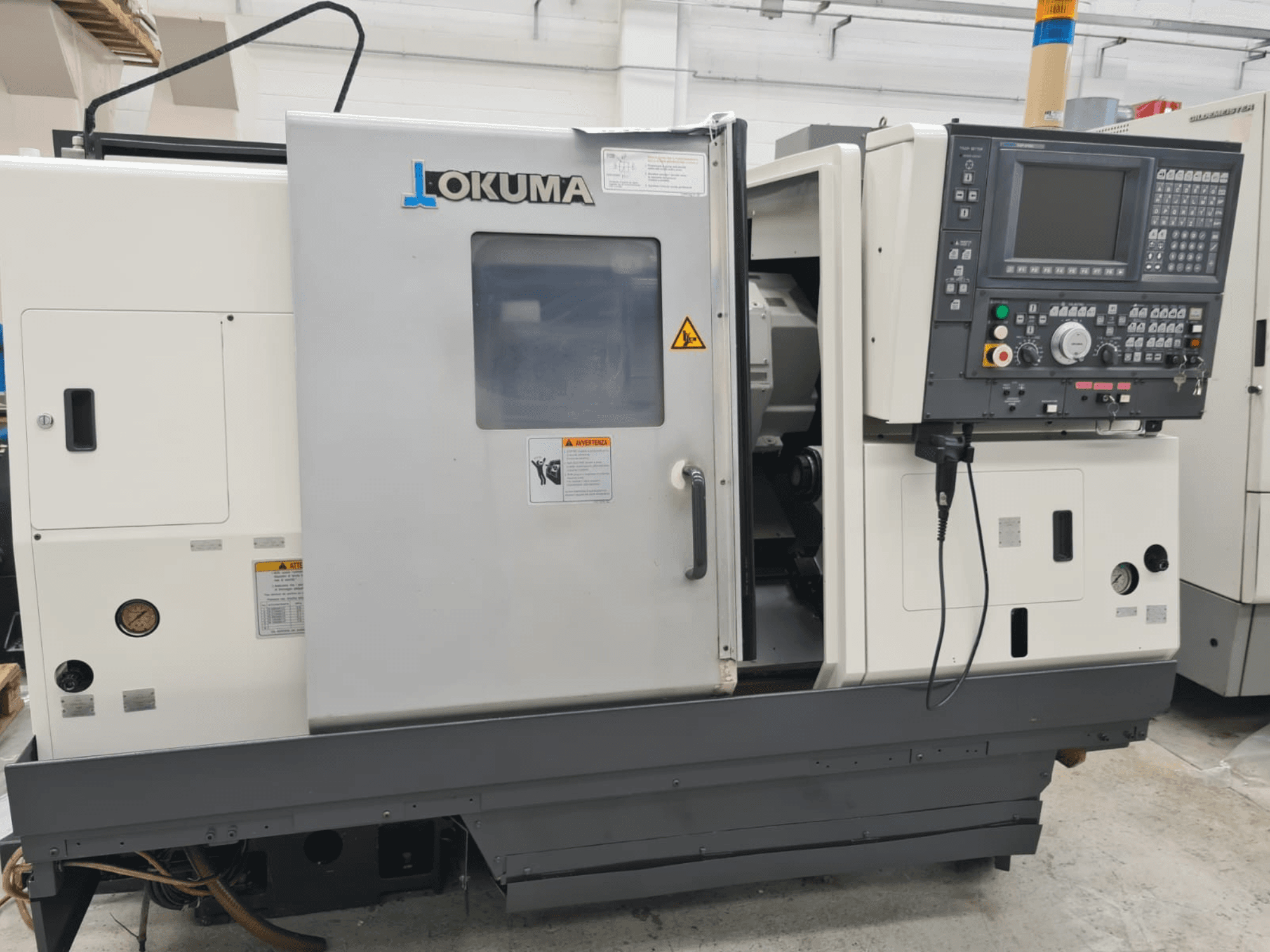 Tornio orizzontale Okuma LB 300M X 500 in vista laterale, con pannello di controllo, accesso al mandrino e avvertenze di sicurezza.