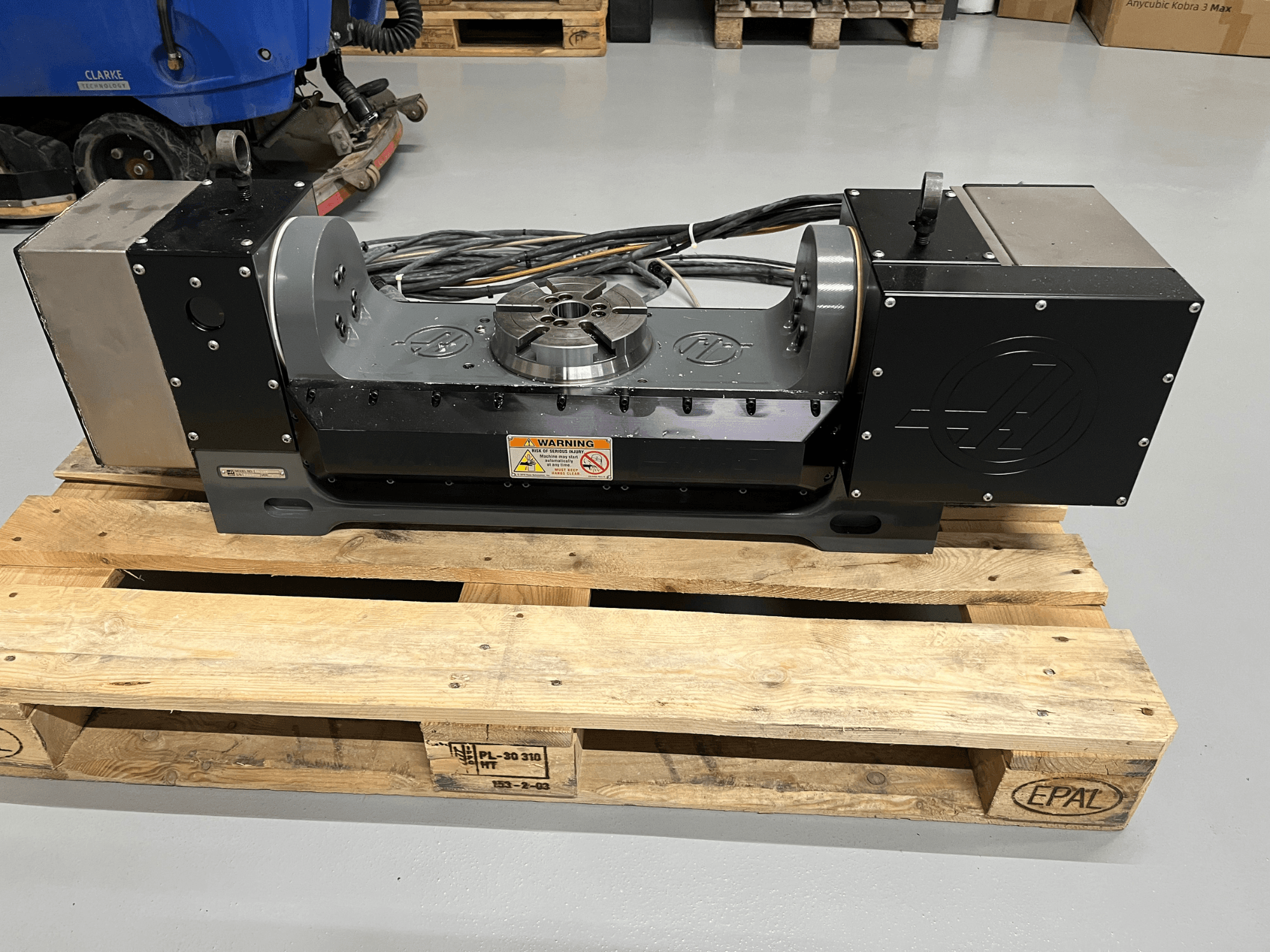 Unità di azionamento del motore dell'asse Z su pallet di legno, vista frontale. Presenta un involucro metallico ed etichette di avvertenza.