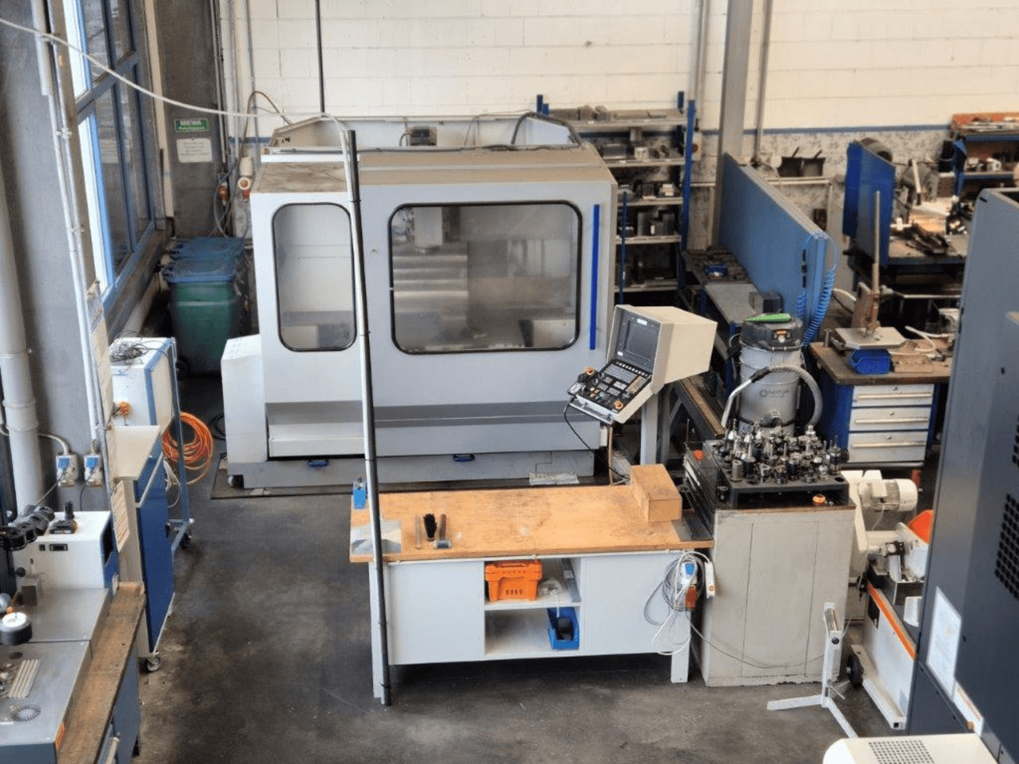 Fresatrice CNC in un'officina, vista frontale, con pannello di controllo, piano di lavoro e utensili visibili sullo sfondo.