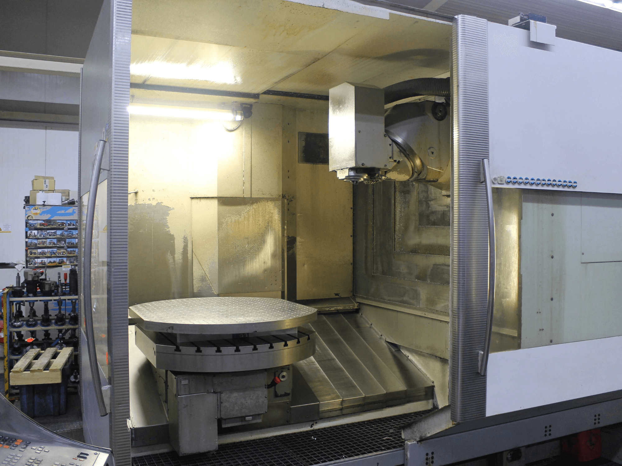 Fresatrice CNC con tavola rotante circolare e testa di taglio, vista frontalmente, con superfici metalliche e illuminazione.