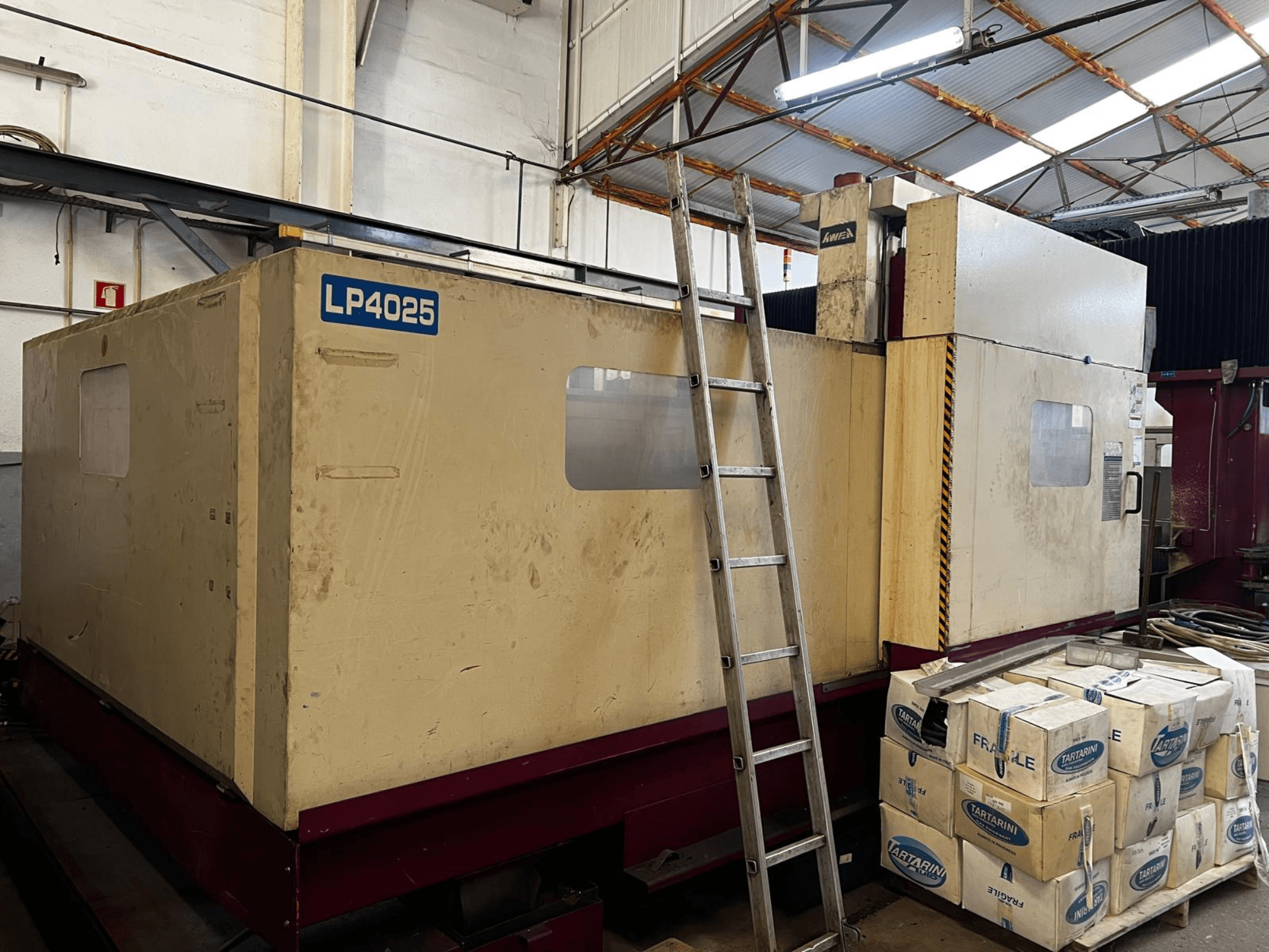 Fresatrice a portale AWEA LP4025 in un ambiente industriale; vista laterale che mostra i grandi macchinari e i contenitori di stoccaggio.