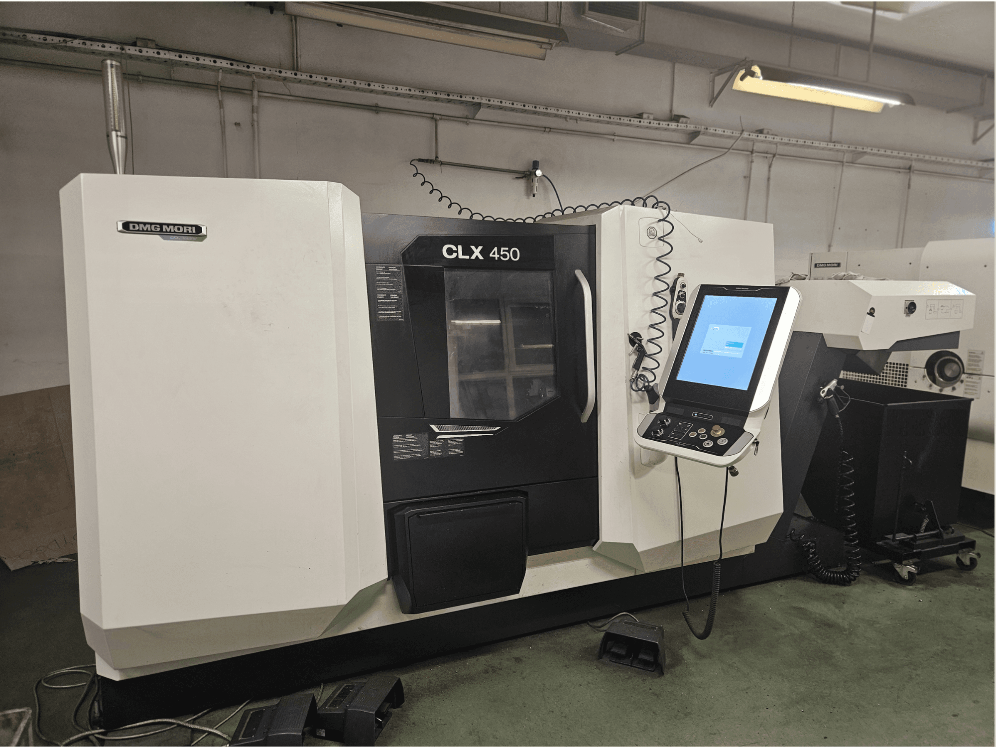 Macchina CNC DMG MORI CLX 450 in vista frontale, con pannello di controllo e display touchscreen, ambientata in un'officina.