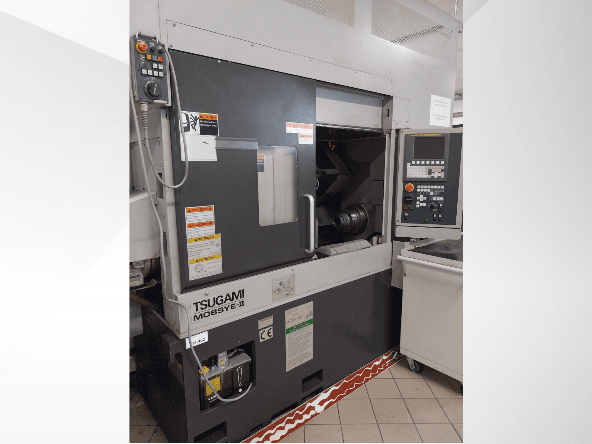 Tornio CNC Tsugami M08SY-II, vista frontale, con pannello di controllo, mandrino e area di carico. Avvisi di sicurezza ed etichetta del marchio.