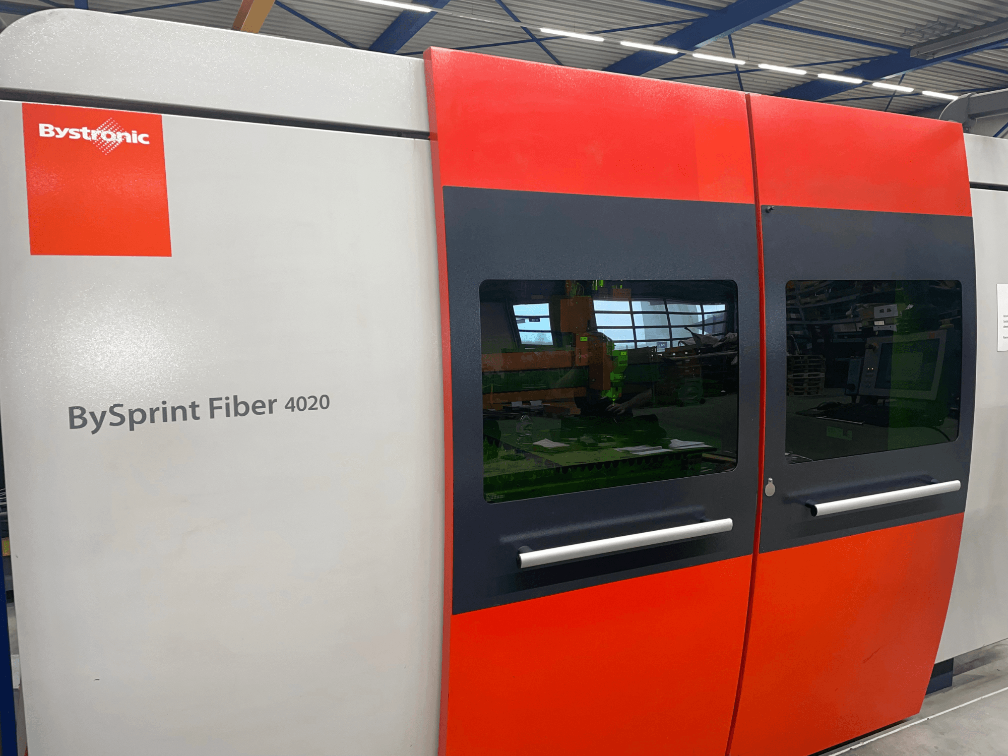 Bystronic BySprint Fiber 4020 in vista frontale, con un design a pannelli grigi e rossi con ampie finestre e interfaccia di controllo visibile all'interno.