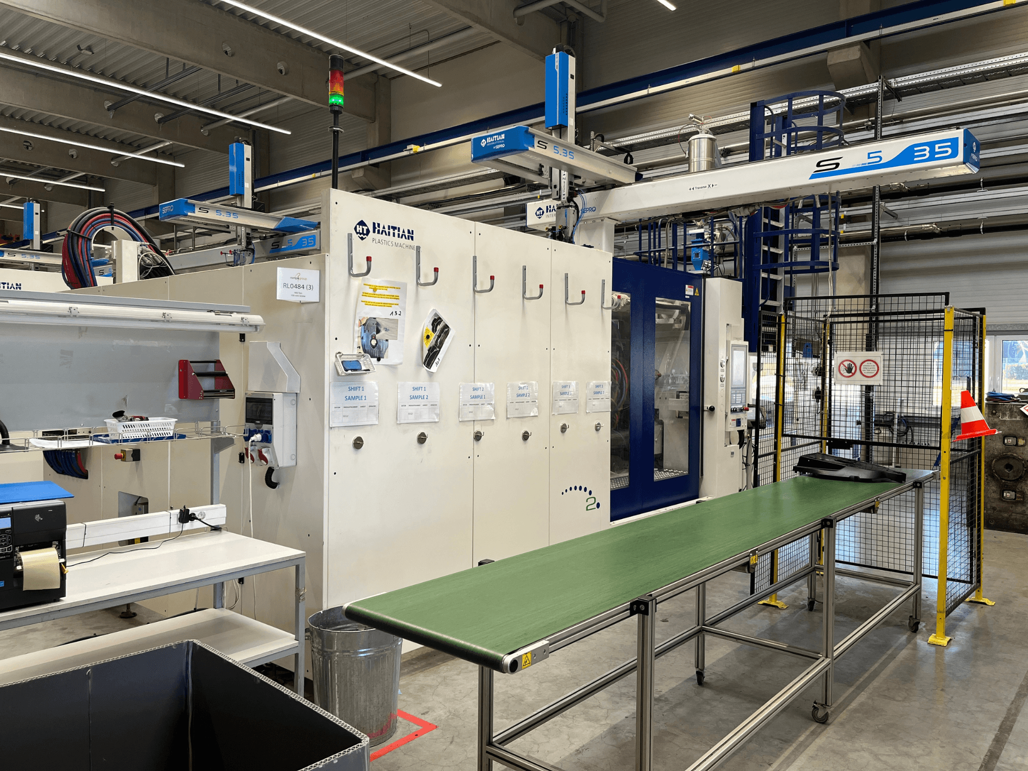 Macchina per plastica S5-35 di Haiti in un'officina; tavolo trasportatore verde, barriere di sicurezza e pannello di controllo visibili dalla vista frontale.
