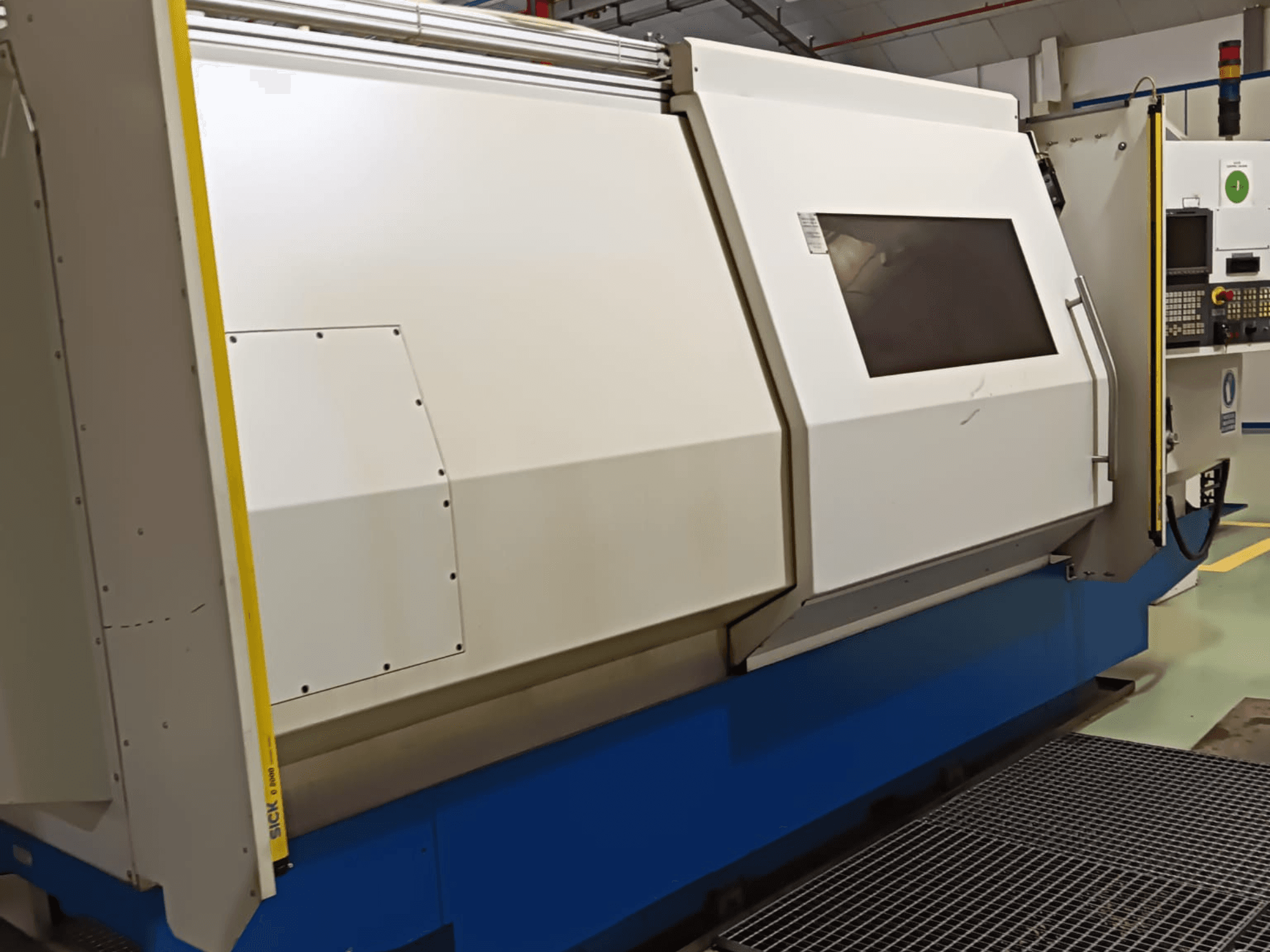 Tornio industriale, vista laterale, caratterizzato da un ampio involucro bianco e blu, pannello di controllo digitale e funzioni di sicurezza.