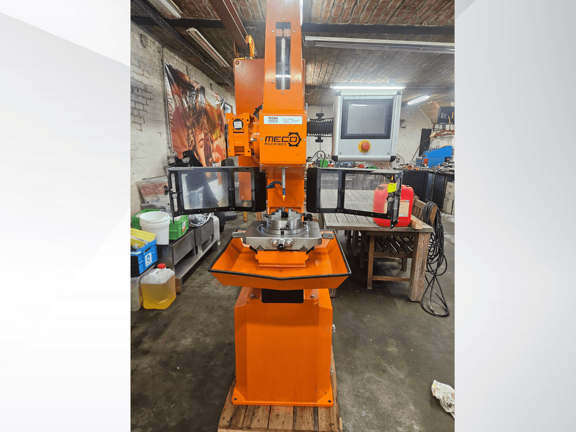 Fresatrice MEC arancione, vista frontale, con pannello di controllo e piano di lavoro, situata in un'officina con utensili e materiali.