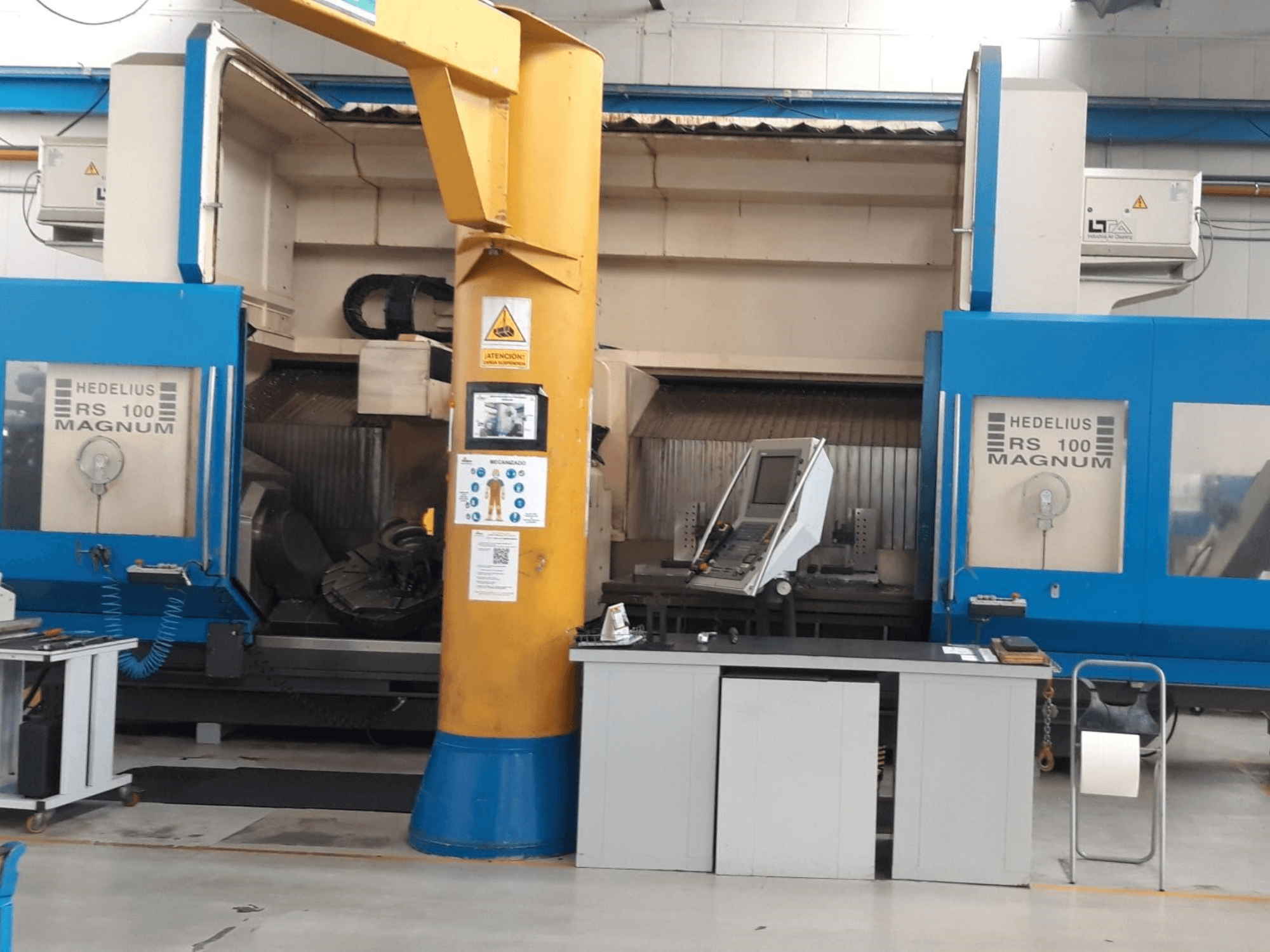 Macchina HEDALIUS RS 100 MAGNUM, vista frontale; presenta il pannello di controllo e la colonna di supporto gialla, in un'area di lavoro industriale.