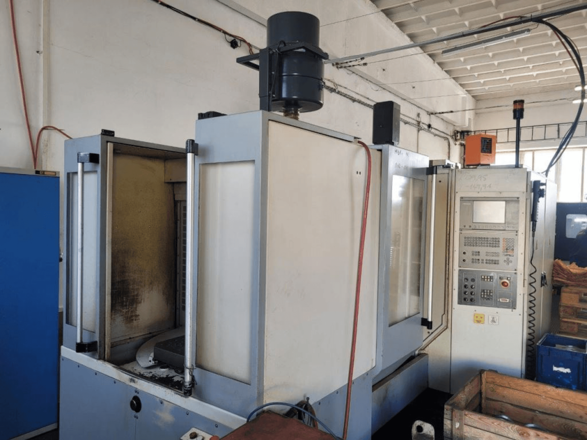 Fresatrice industriale a controllo numerico con pannello di controllo, vista laterale, che mostra l'involucro e lo sporco visibile sulle superfici.