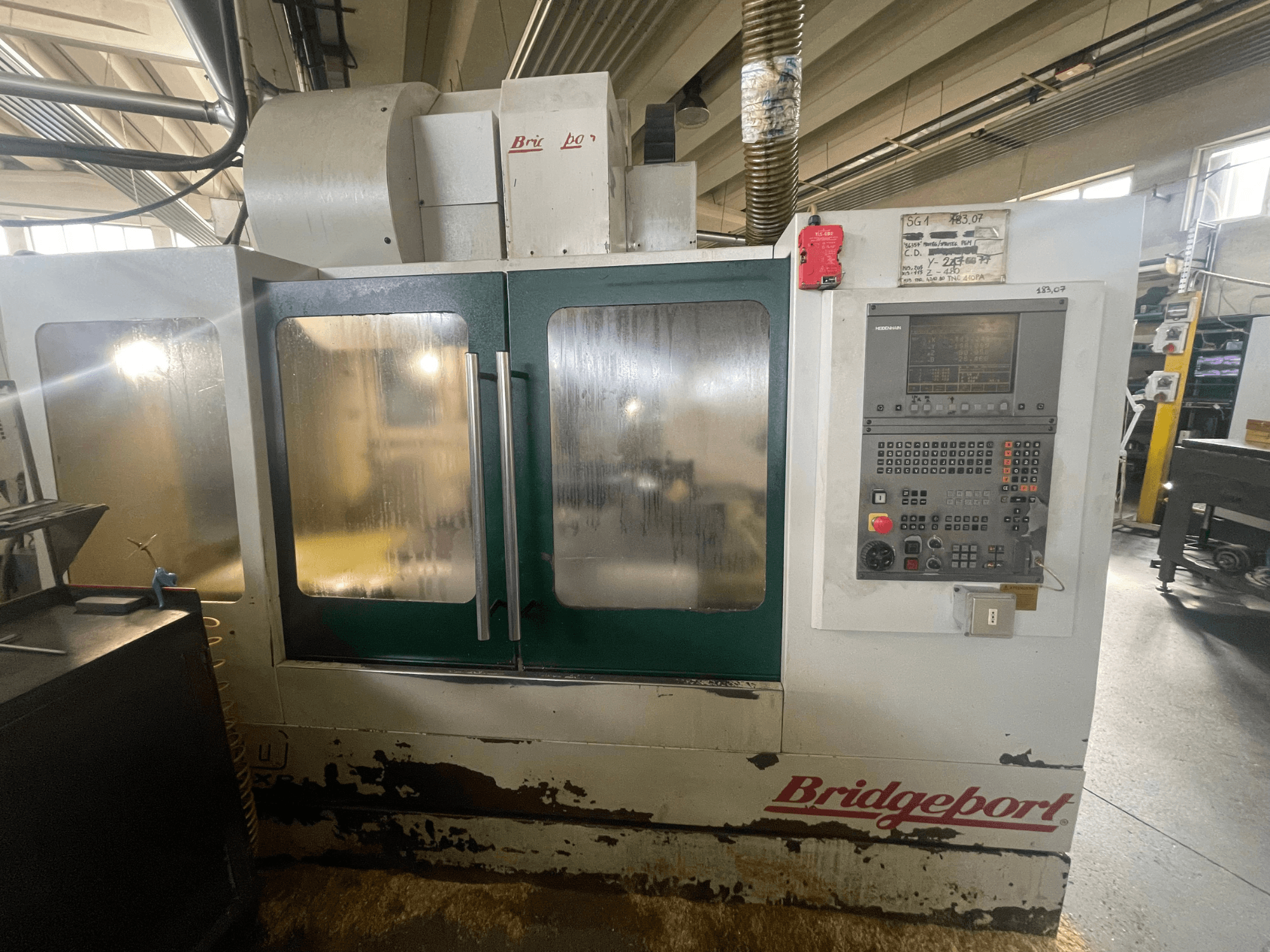 Centro di lavorazione verticale Bridgeport VMC 1000/30, vista frontale con pannello di controllo, che mostra la carrozzeria usurata e le porte verdi.
